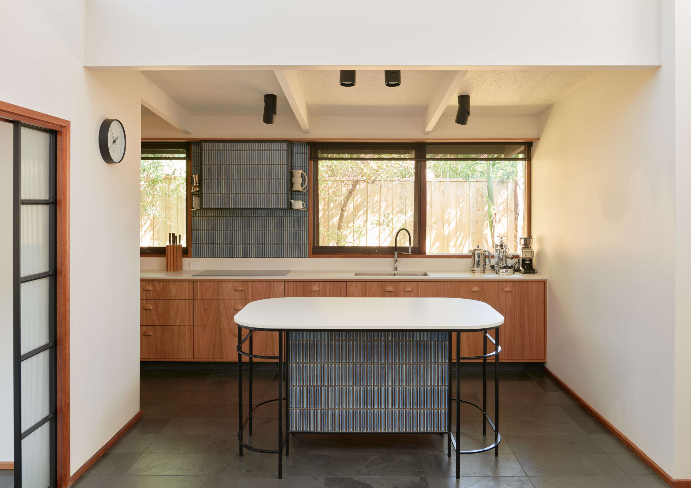 Mid-century inspired kitchen with timber joinery, dark tiled island, and expansive rear glazing.