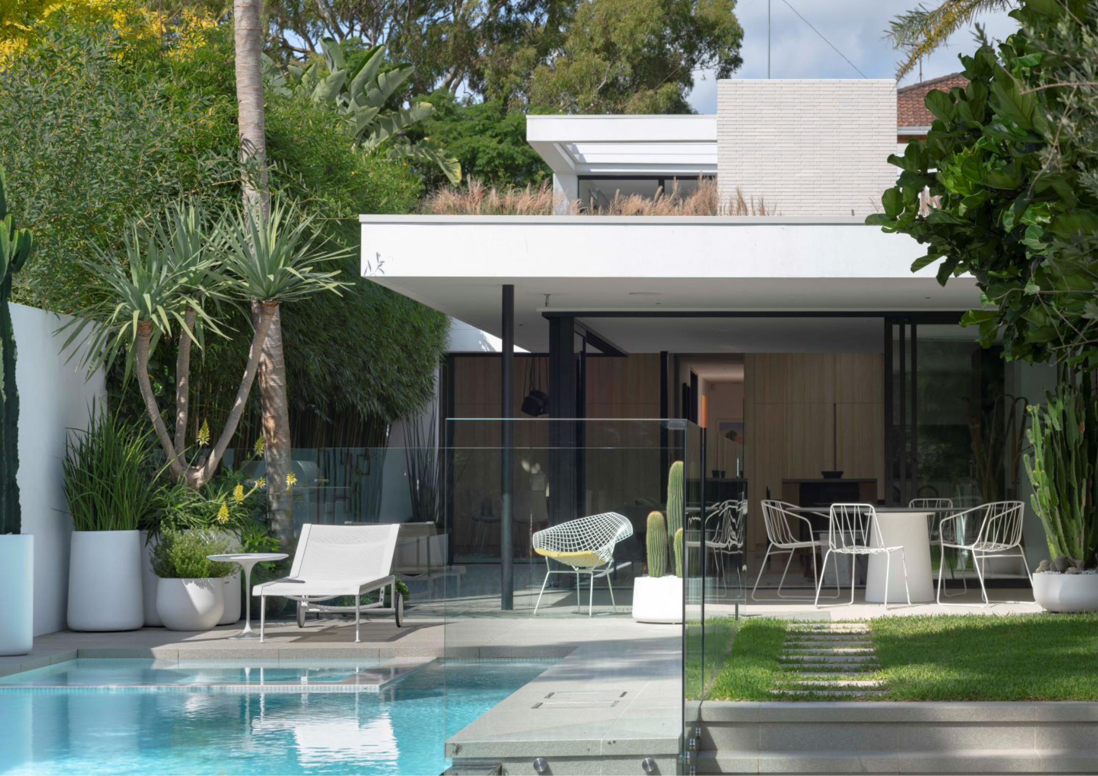 Modern courtyard house with white horizontal roof planes, open-plan living spaces, glass balustrades, and poolside terrace surrounded by tropical planting.