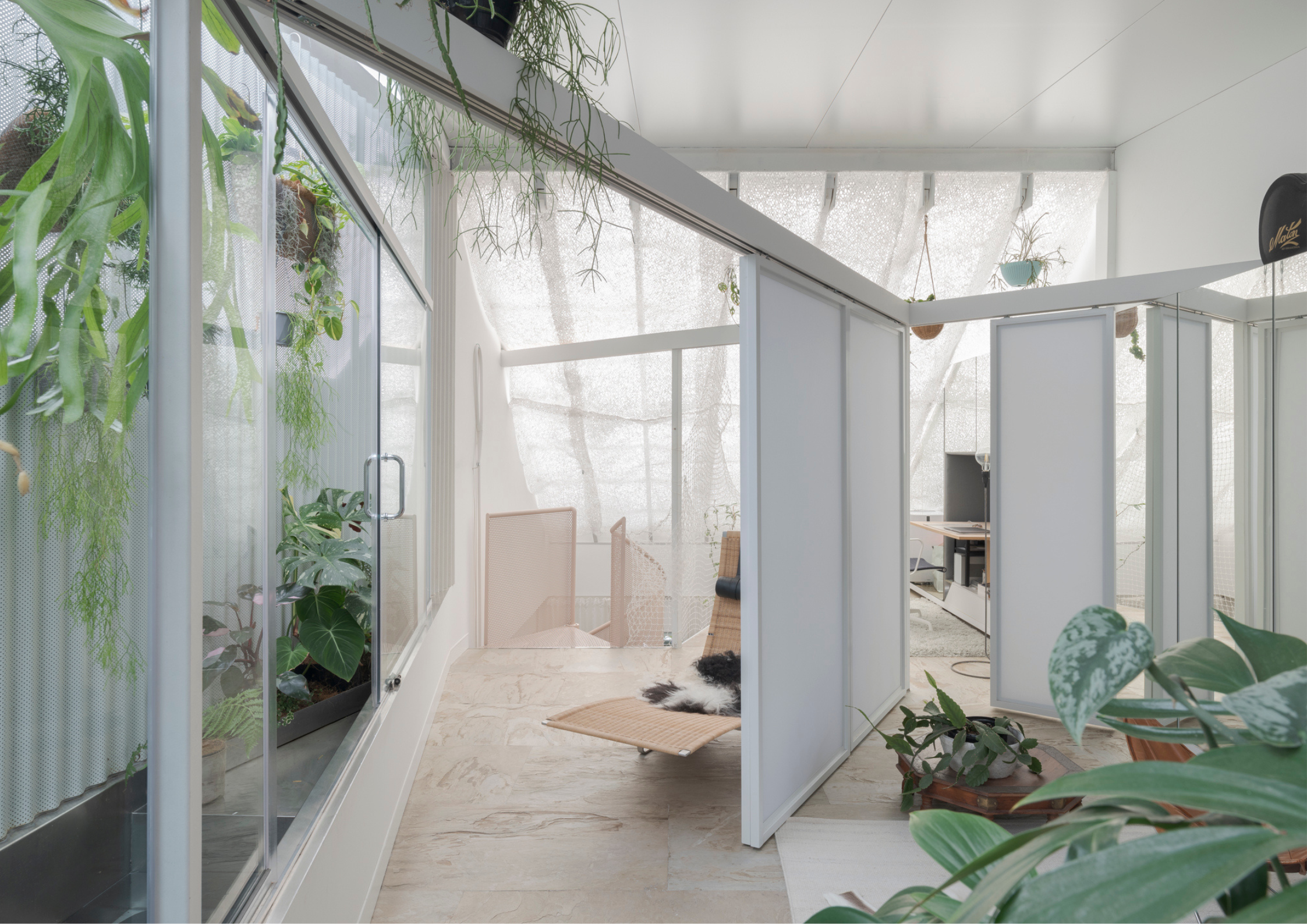 Bright light-filled interior workspace with translucent sliding partitions, indoor greenery, perforated screening, and soft natural light filtering throughout the space.