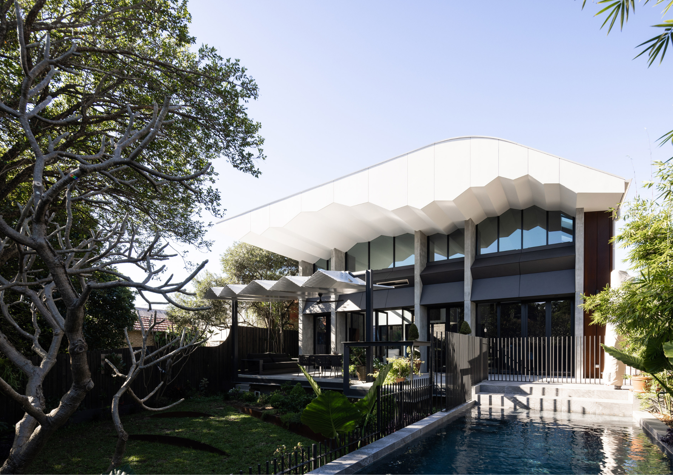 Sculptural contemporary home with curved white roofline, rhythmic concrete columns, expansive glazing, and landscaped pool courtyard.