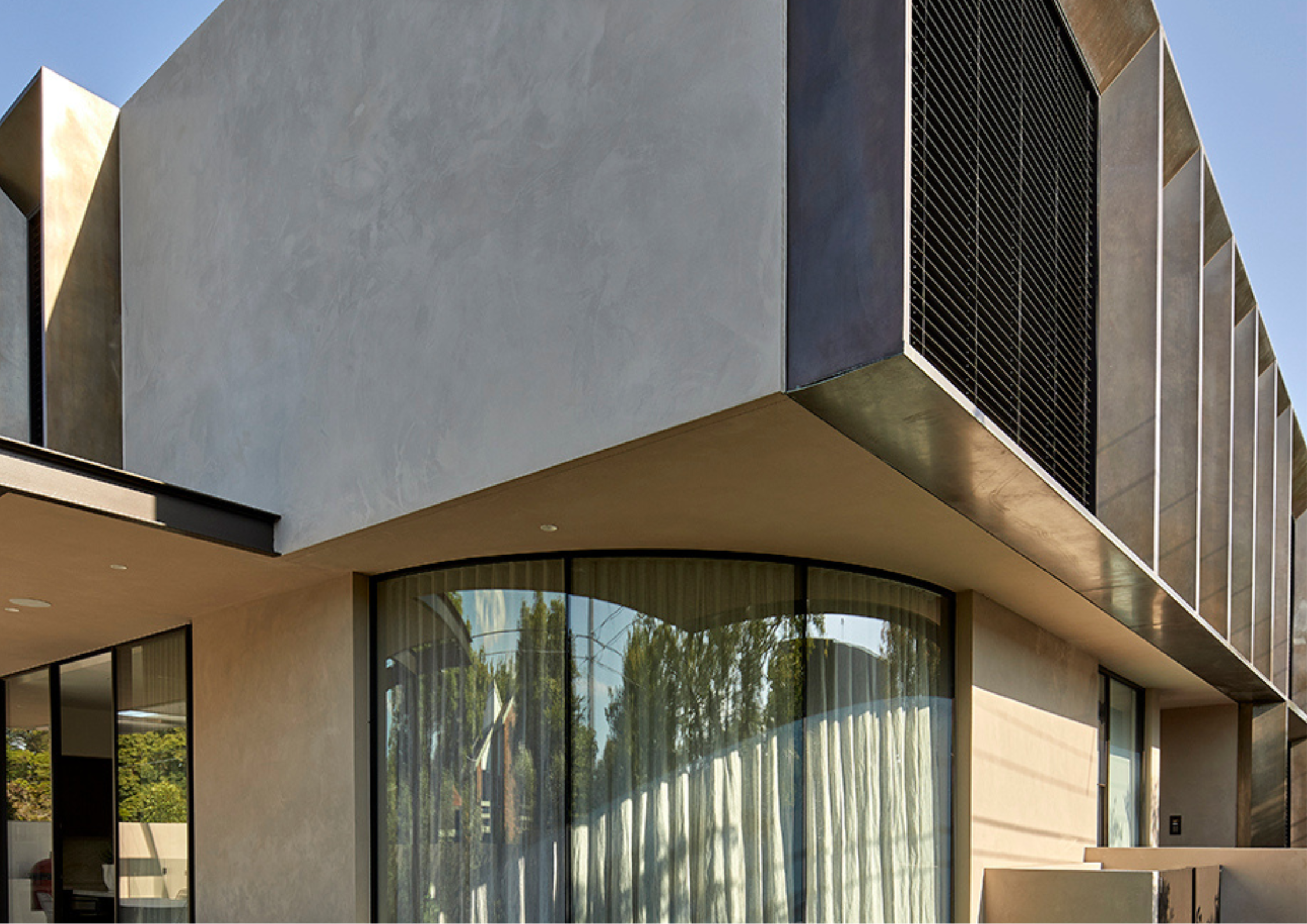 Modern home exterior with curved glass corner, textured walls, and metal screening.