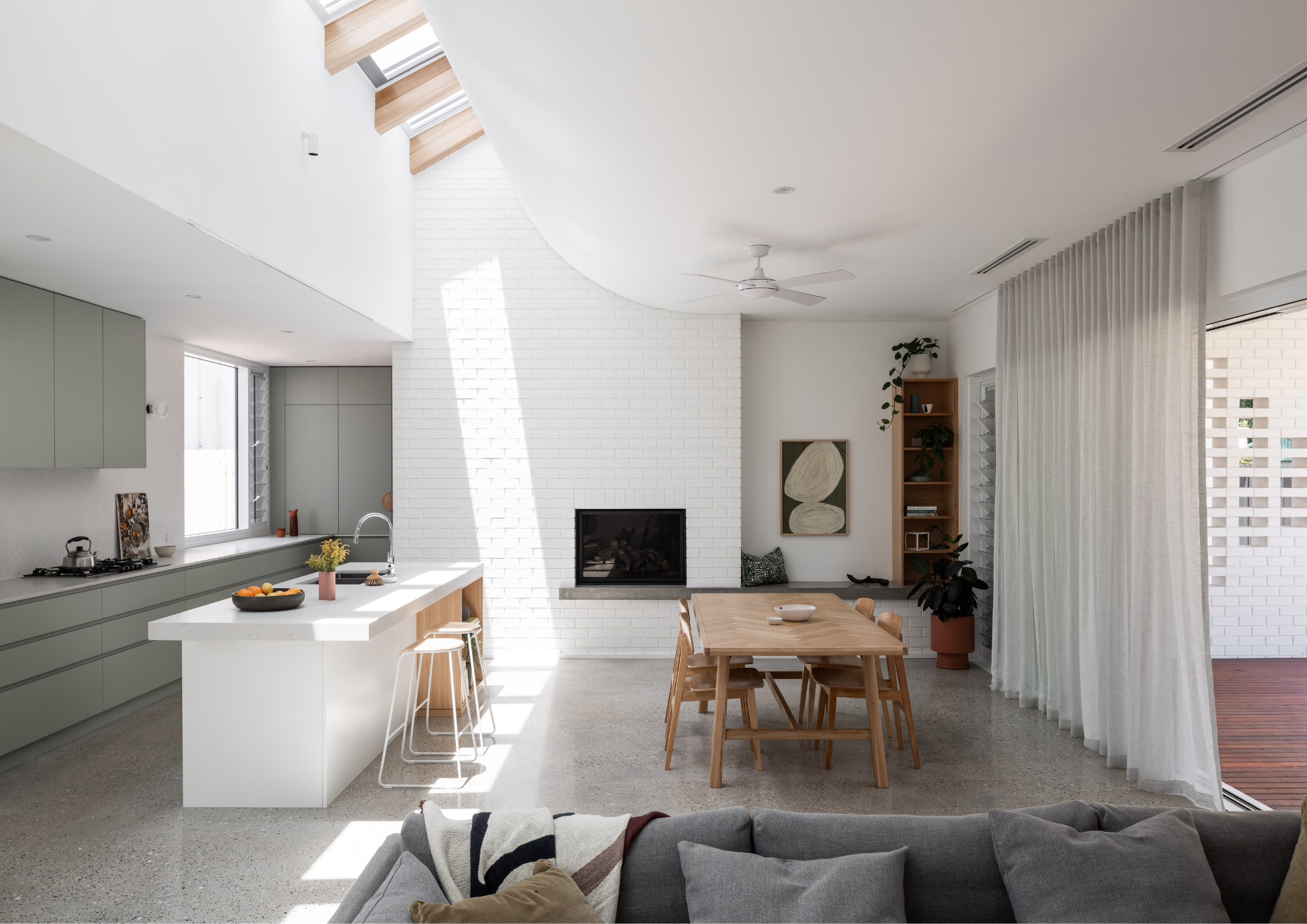 Bright open-plan kitchen and dining area with curved white ceilings, skylights, polished concrete floors, and minimalist detailing.