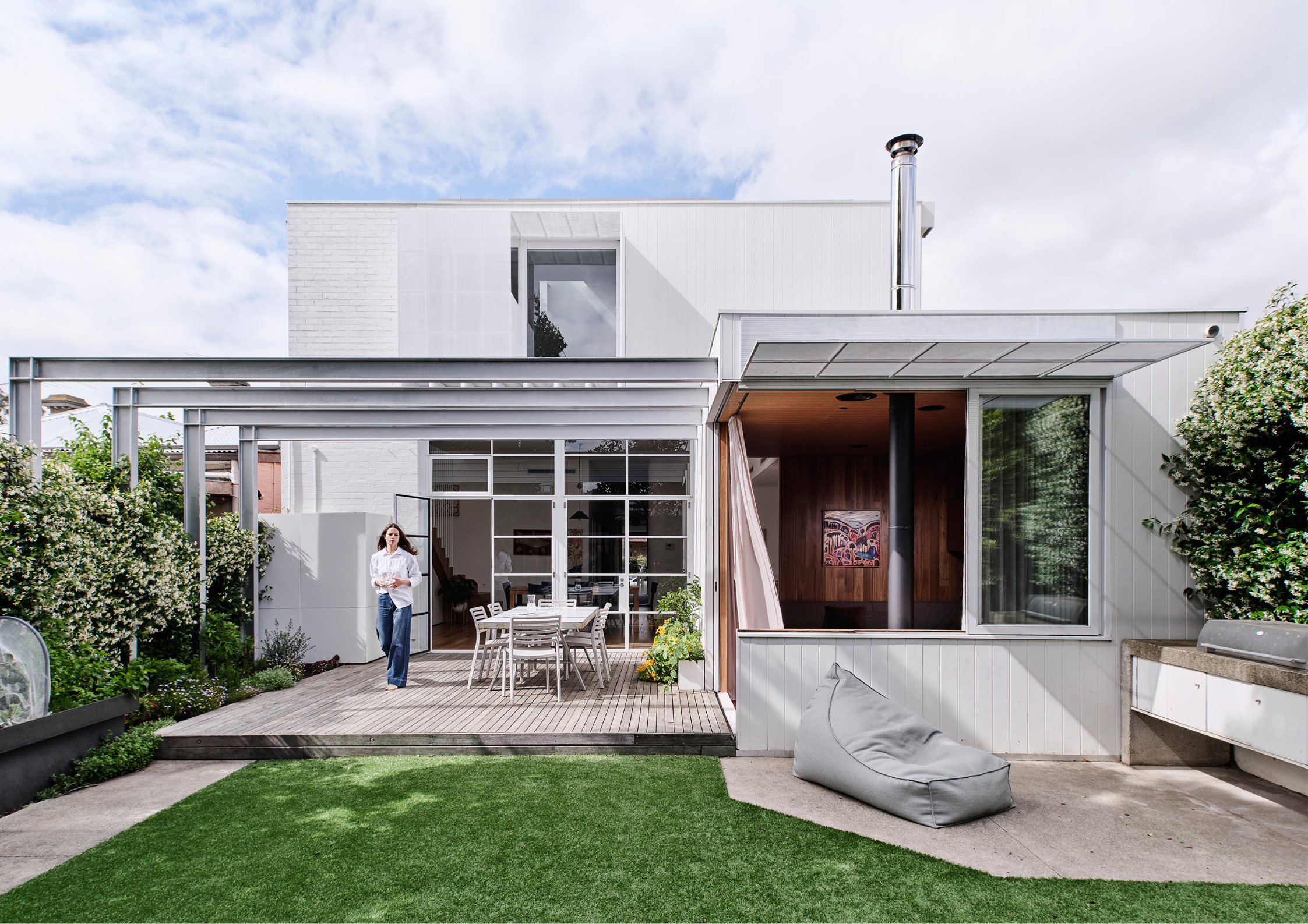 A contemporary home extension with a timber deck, outdoor dining area, and large glass doors opening to a garden.