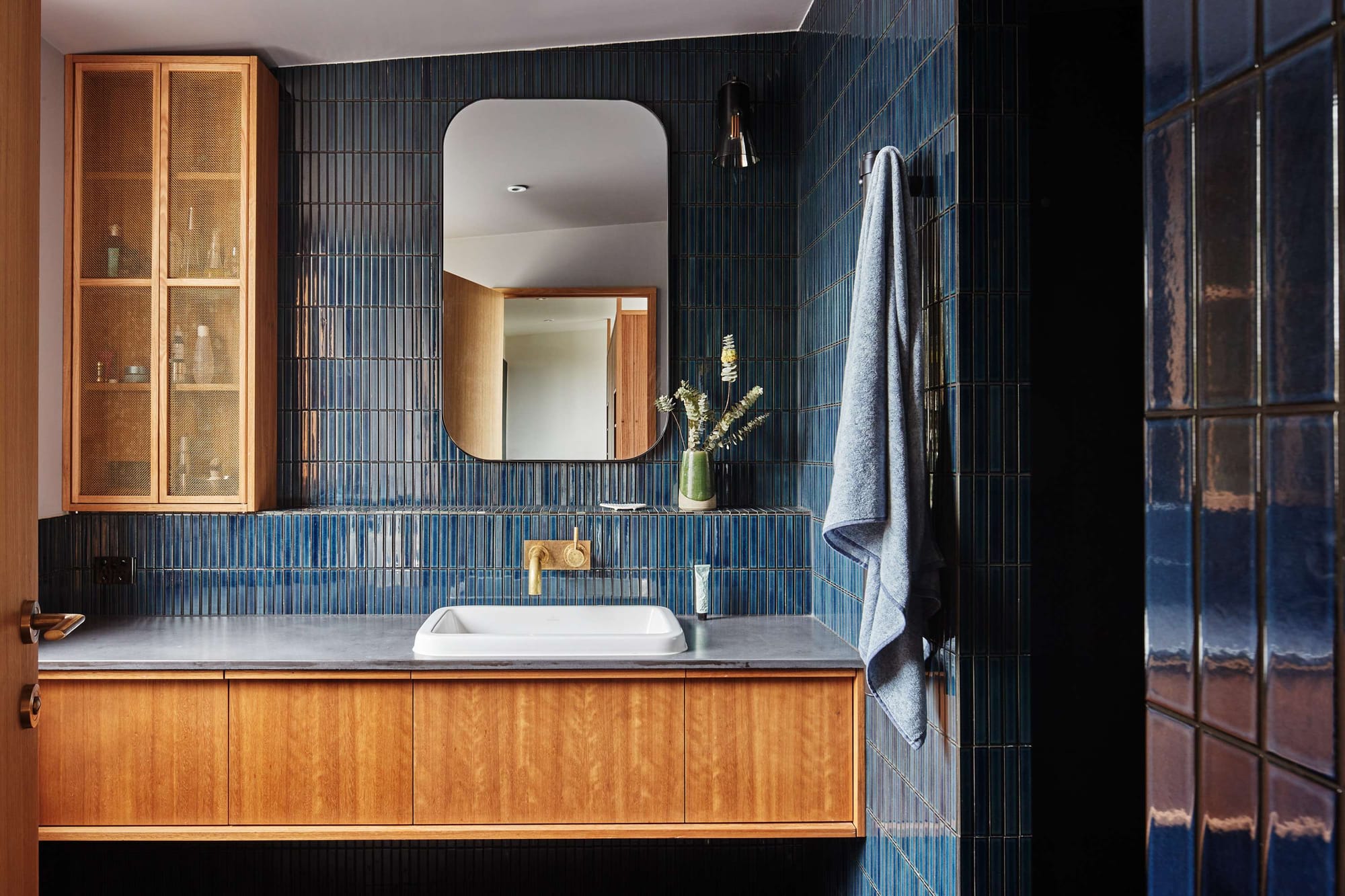Deep blue tiled bathroom with timber vanity, brass tapware and textured glossy wall tiles.