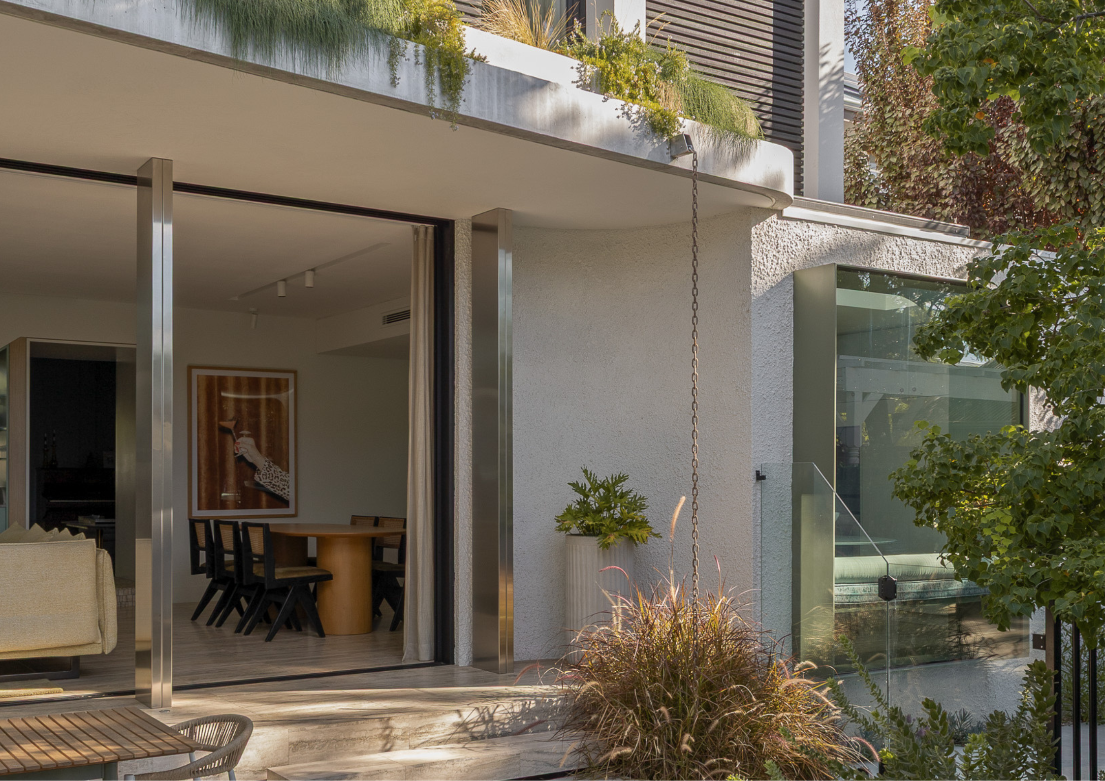 Contemporary indoor-outdoor living area with textured concrete finishes, landscaped balcony planting, and floor-to-ceiling sliding glass doors.