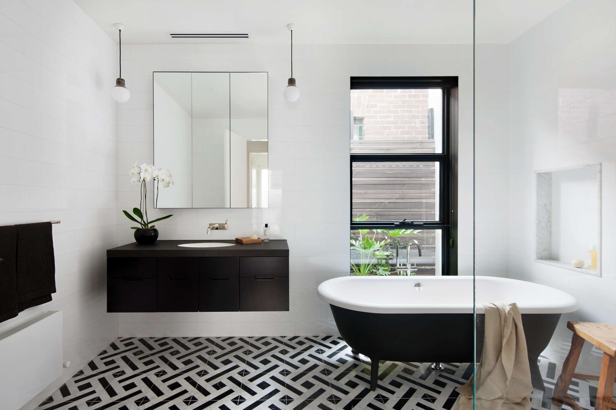 Contemporary black and white bathroom with geometric floor tiles, freestanding bathtub and minimalist black vanity.