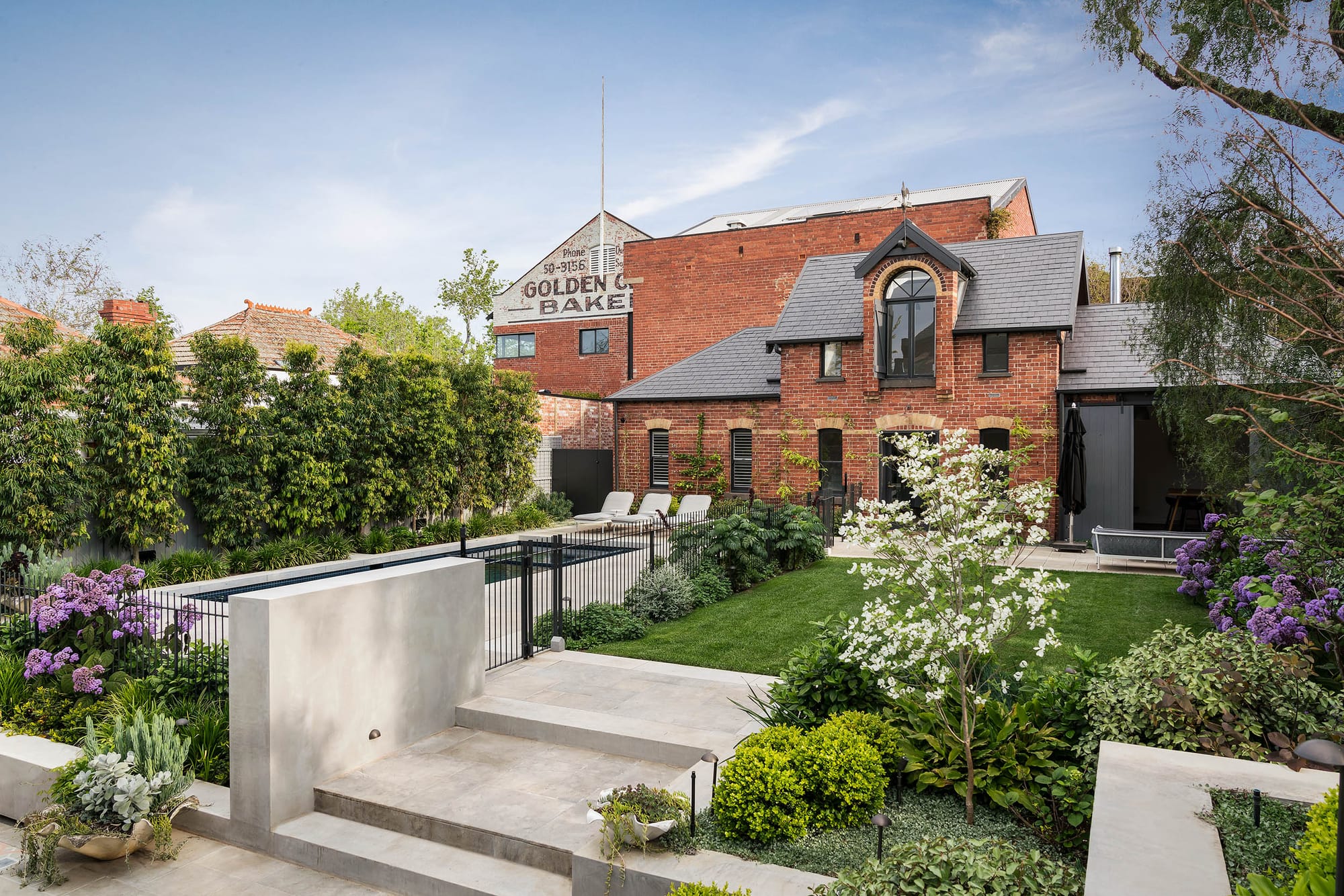 Rear garden of the Armadale residence by Myles Baldwin Design, with terraced limestone paving, a pool, manicured lawn and abundant flowering planting including hydrangeas and ornamental trees