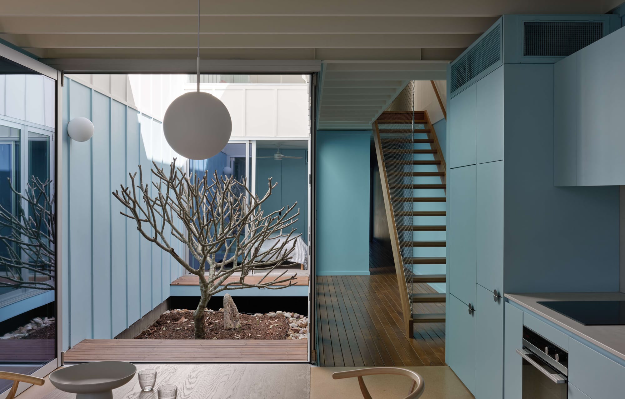 Interior view of kitchen and central garden courtyard with frangipani tree and timber staircase, Blok Three Sisters by Blok Modular