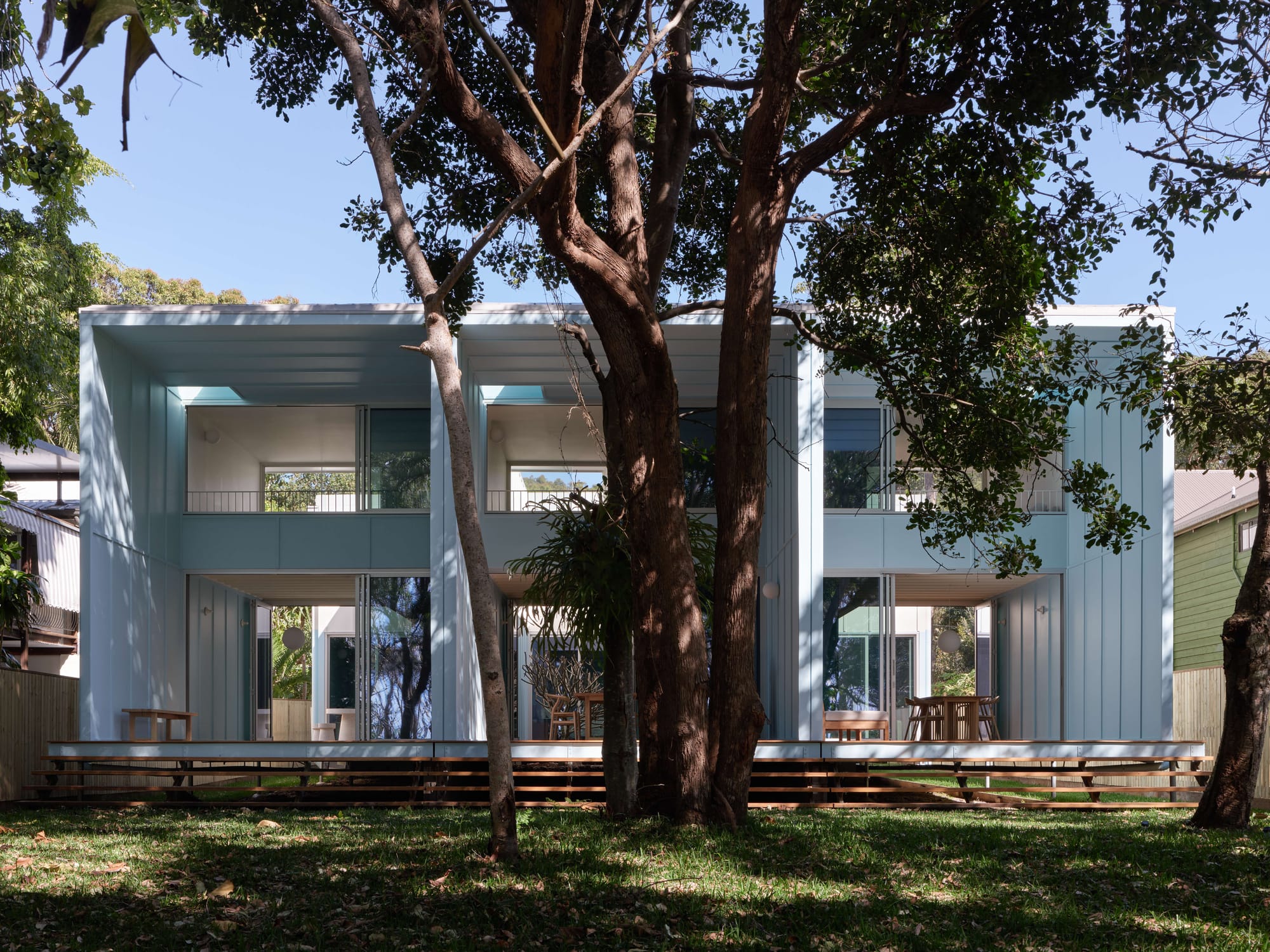 Exterior of three modular coastal terrace houses clad in pale blue, set among mature trees on Minjerribah, Blok Three Sisters by Blok Modular