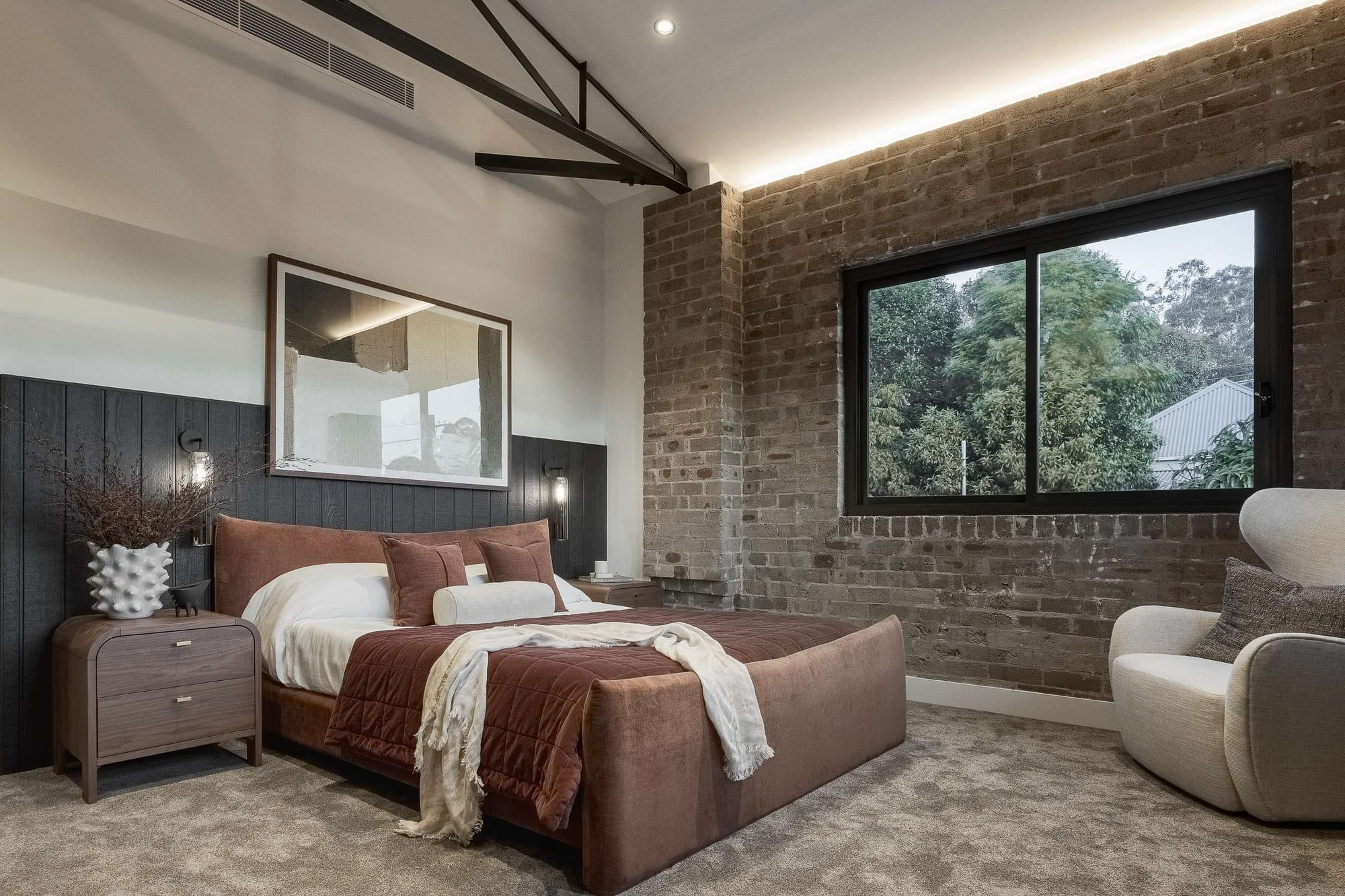 Bedroom in the Foster Street Duplex by BJB Architects featuring original warehouse brick walls, exposed steel roof trusses, dark timber panelling and warm ambient lighting