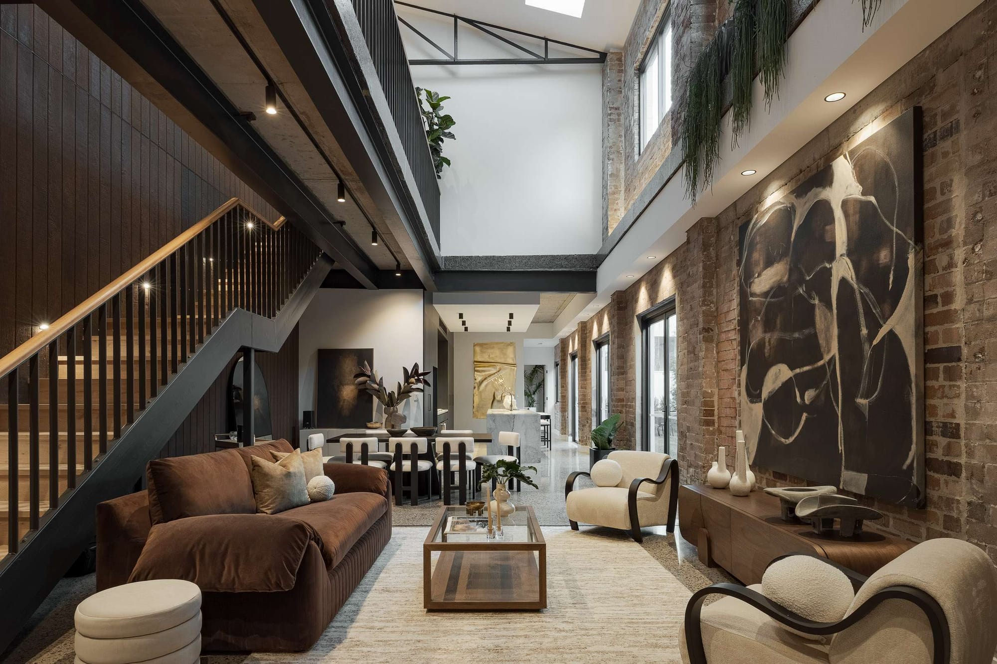 Double-height living space in the Foster Street Duplex by BJB Architects, with original exposed brick walls, steel warehouse trusses, a timber staircase and large-scale artwork