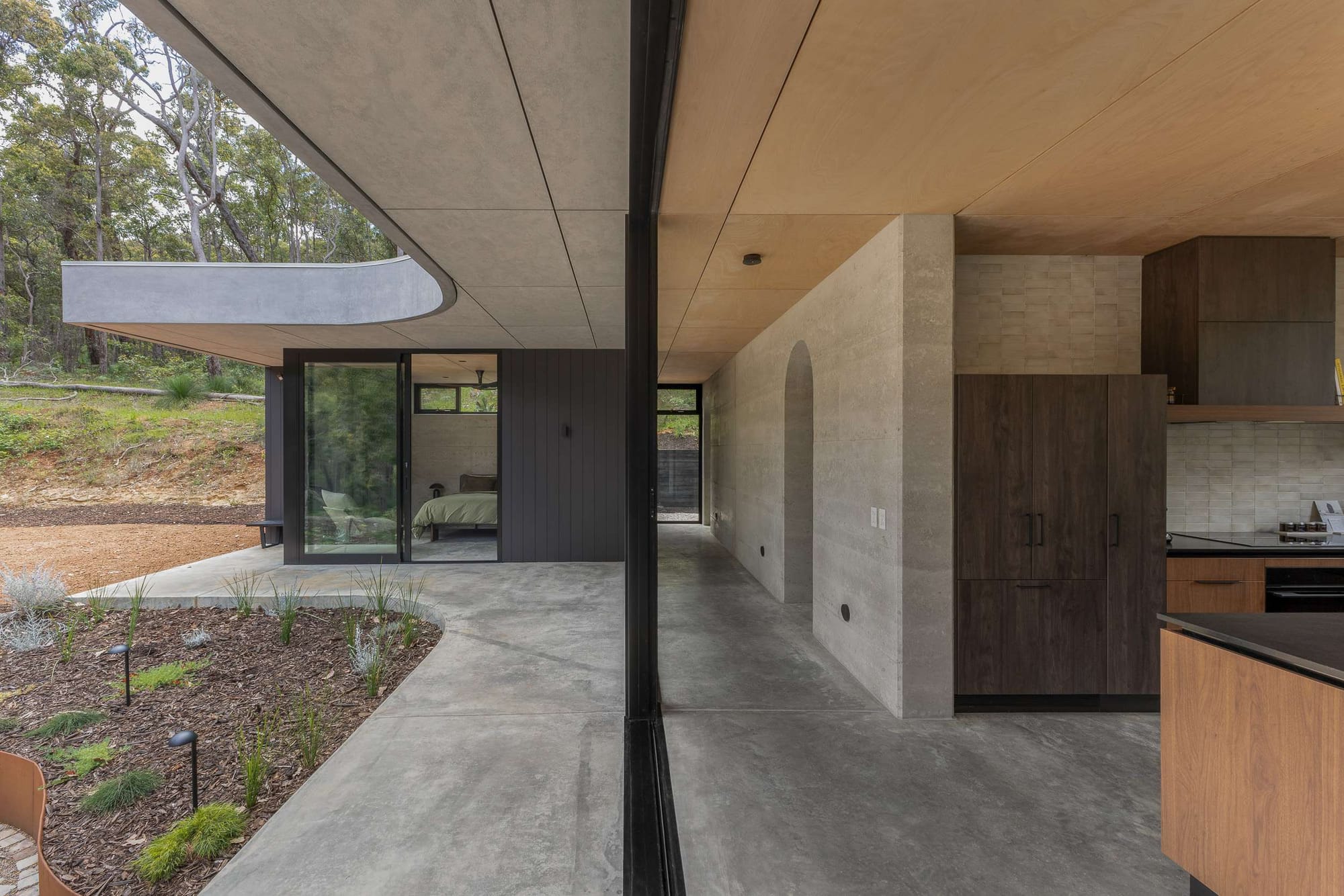 Polished concrete floor runs continuously from an open plan kitchen through to a covered outdoor terrace overlooking native bushland, Gold Gully by Keen Architecture