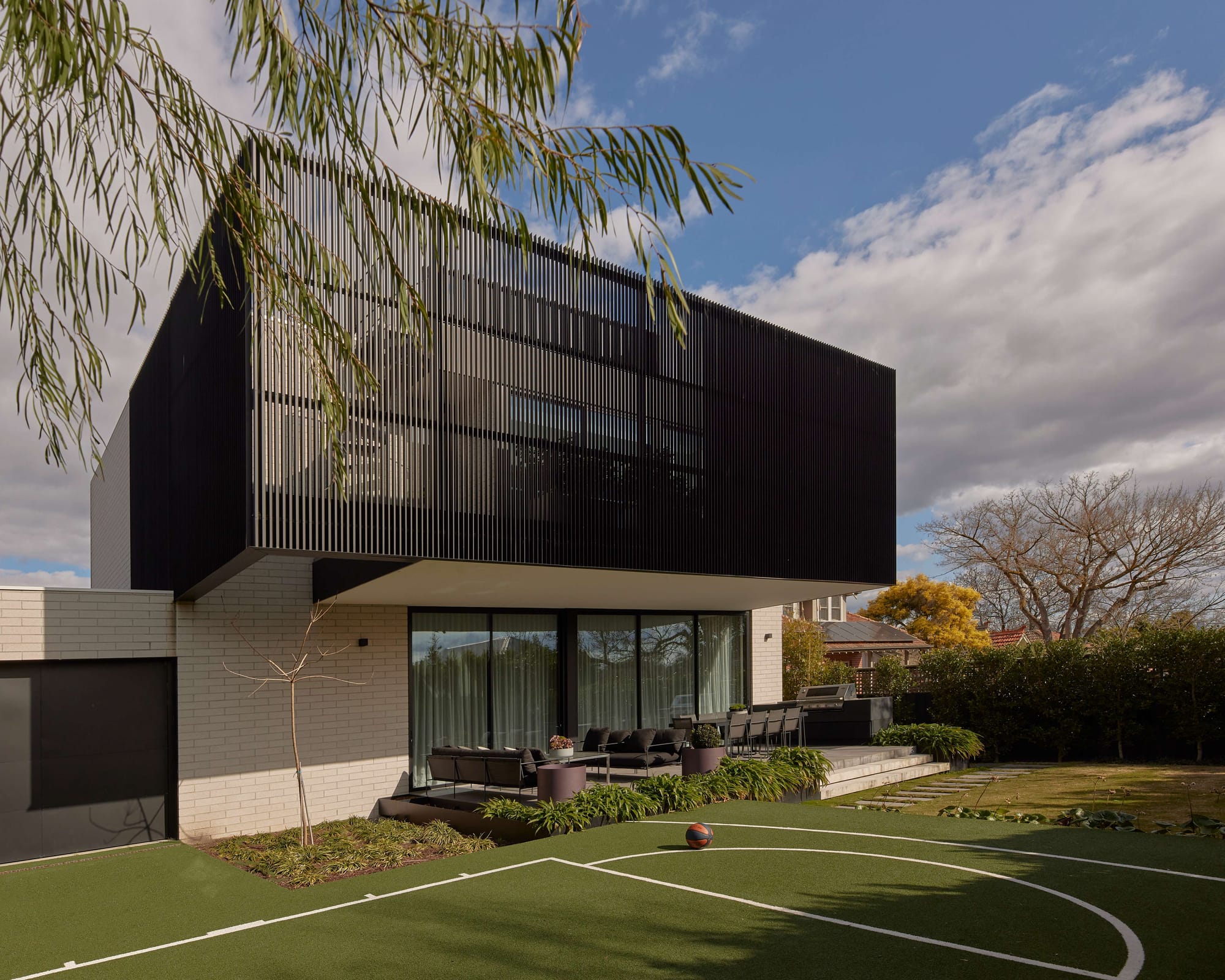Contemporary black louvred addition to Hawthorn East House by Emma Tulloch Architects, with full-height glazing, outdoor entertaining terrace and a backyard basketball court