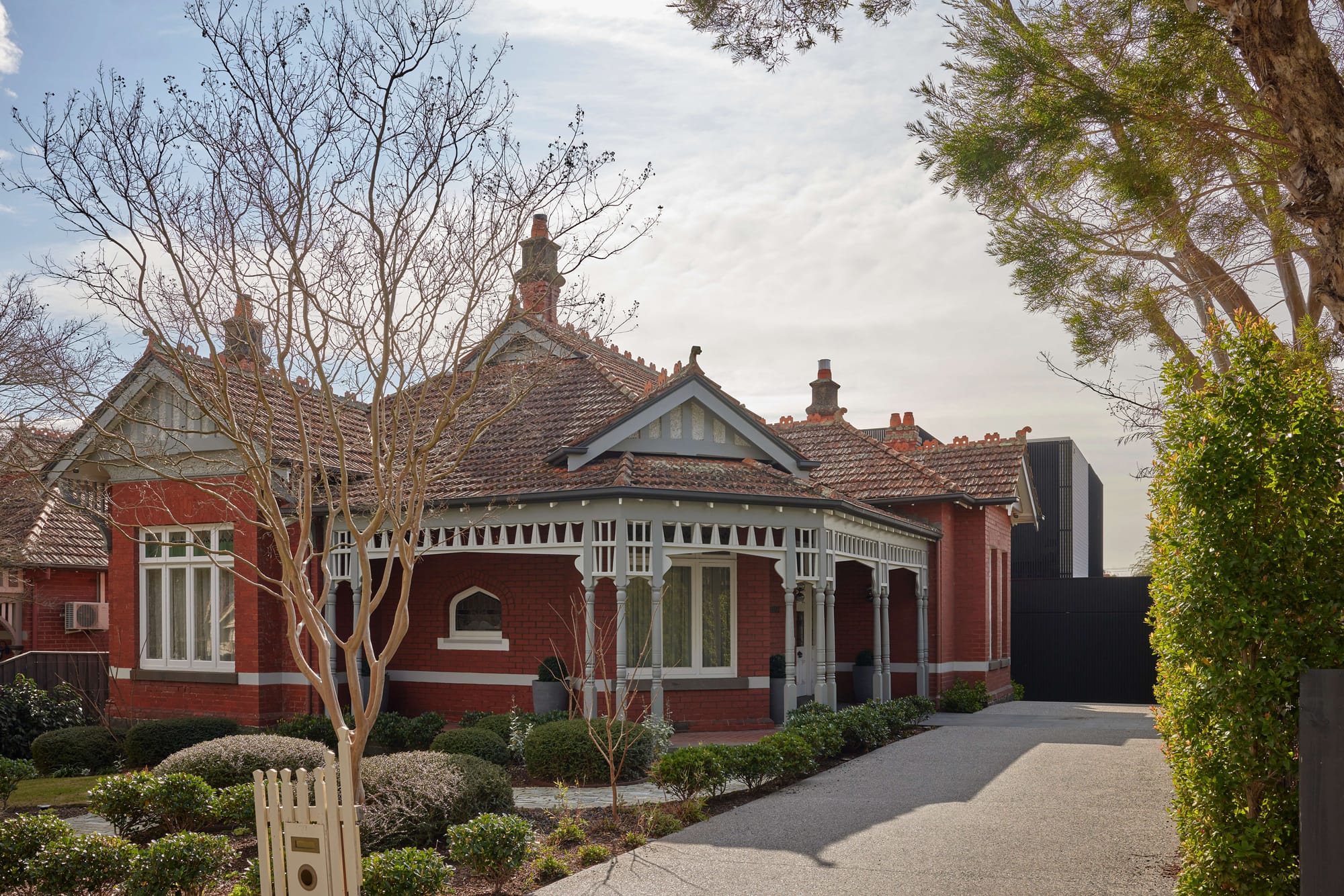 Heritage red brick facade of Hawthorn East House by Emma Tulloch Architects, with ornate Victorian detailing, terracotta roof tiles and a contemporary dark addition visible at the rear