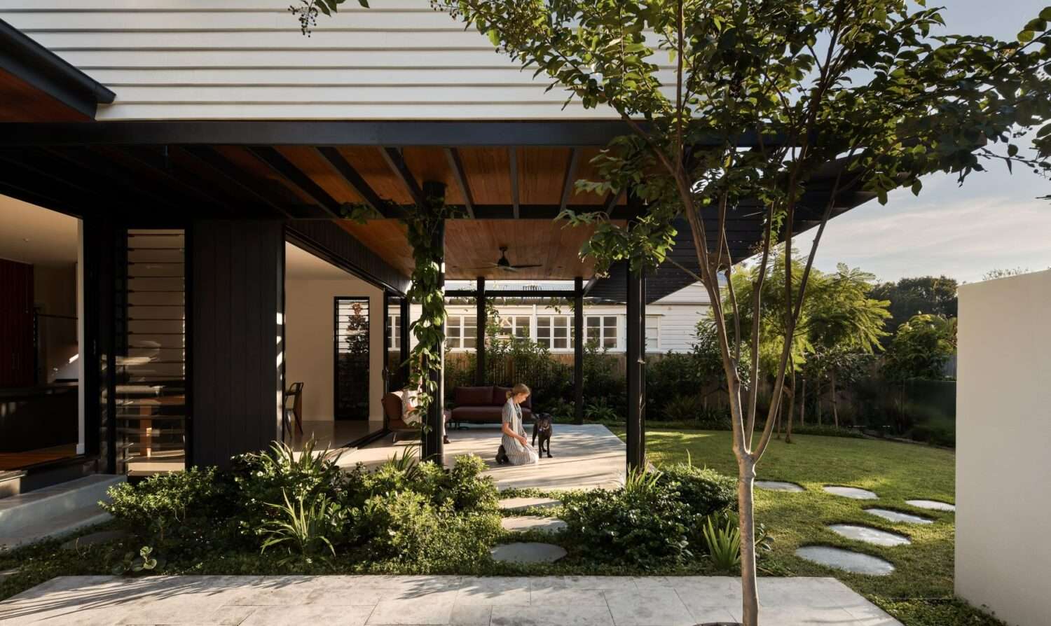 A covered outdoor living pavilion with timber ceiling and ceiling fan connects to a lush garden with stepping stones and established trees, Kalinga Garden House by Alexandra Buchanan Architecture