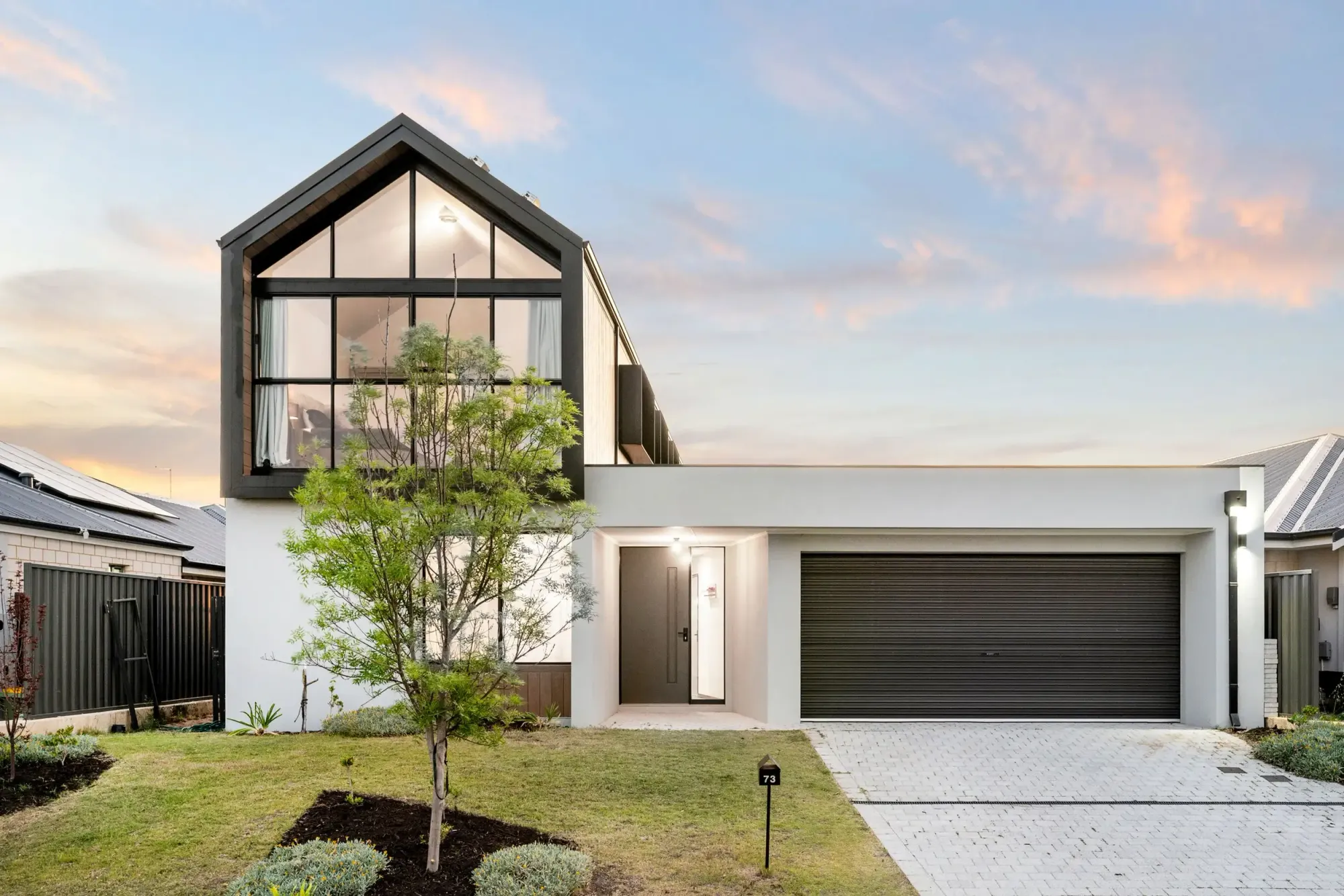 Street facade of Koto House at dusk with barn-inspired gabled upper level and Japanese maple tree, Cynosure Architecture