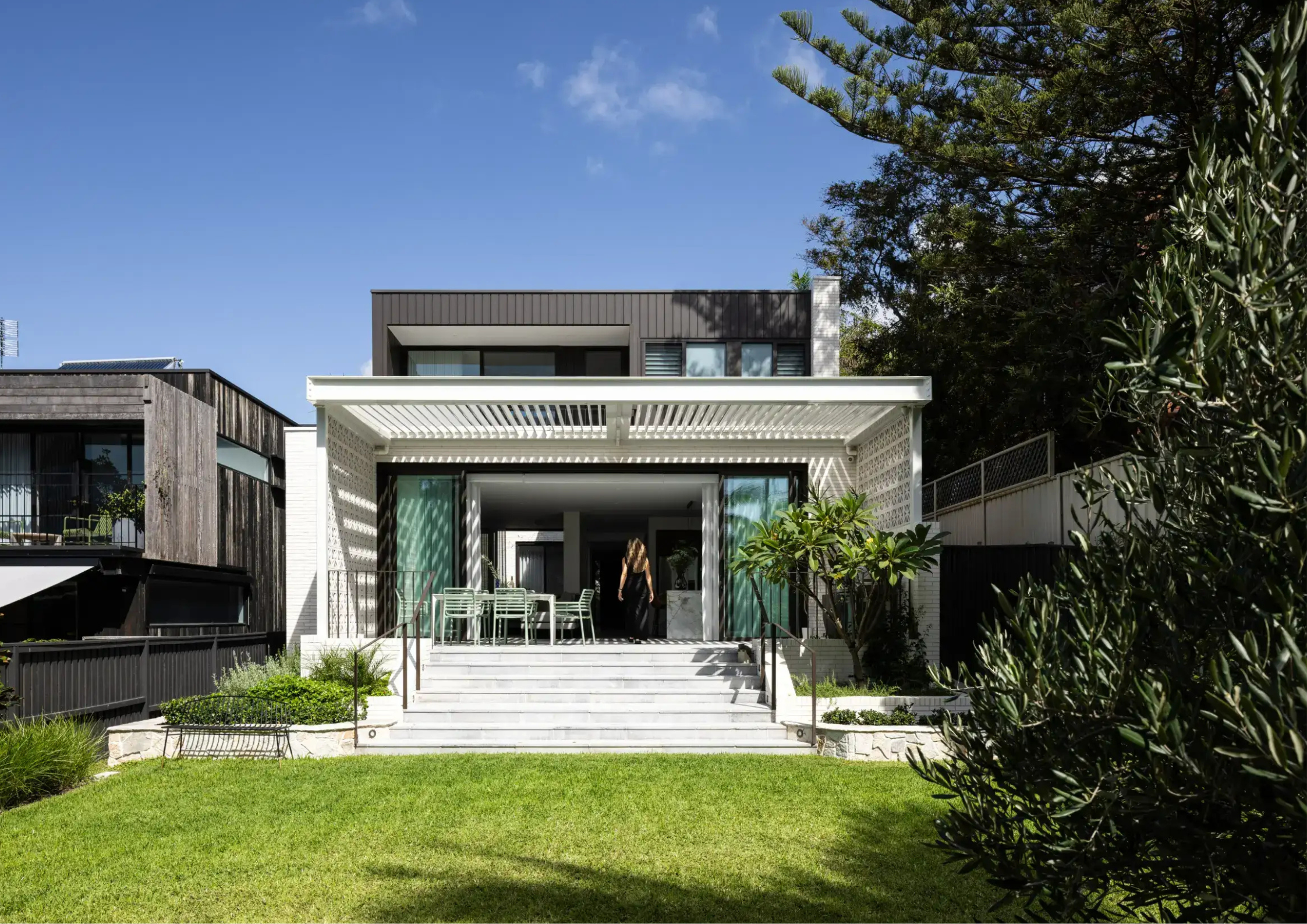 Two-storey home with a louvre pergola over an elevated outdoor entertaining area, marble steps, dining setting, and mature garden surrounds.