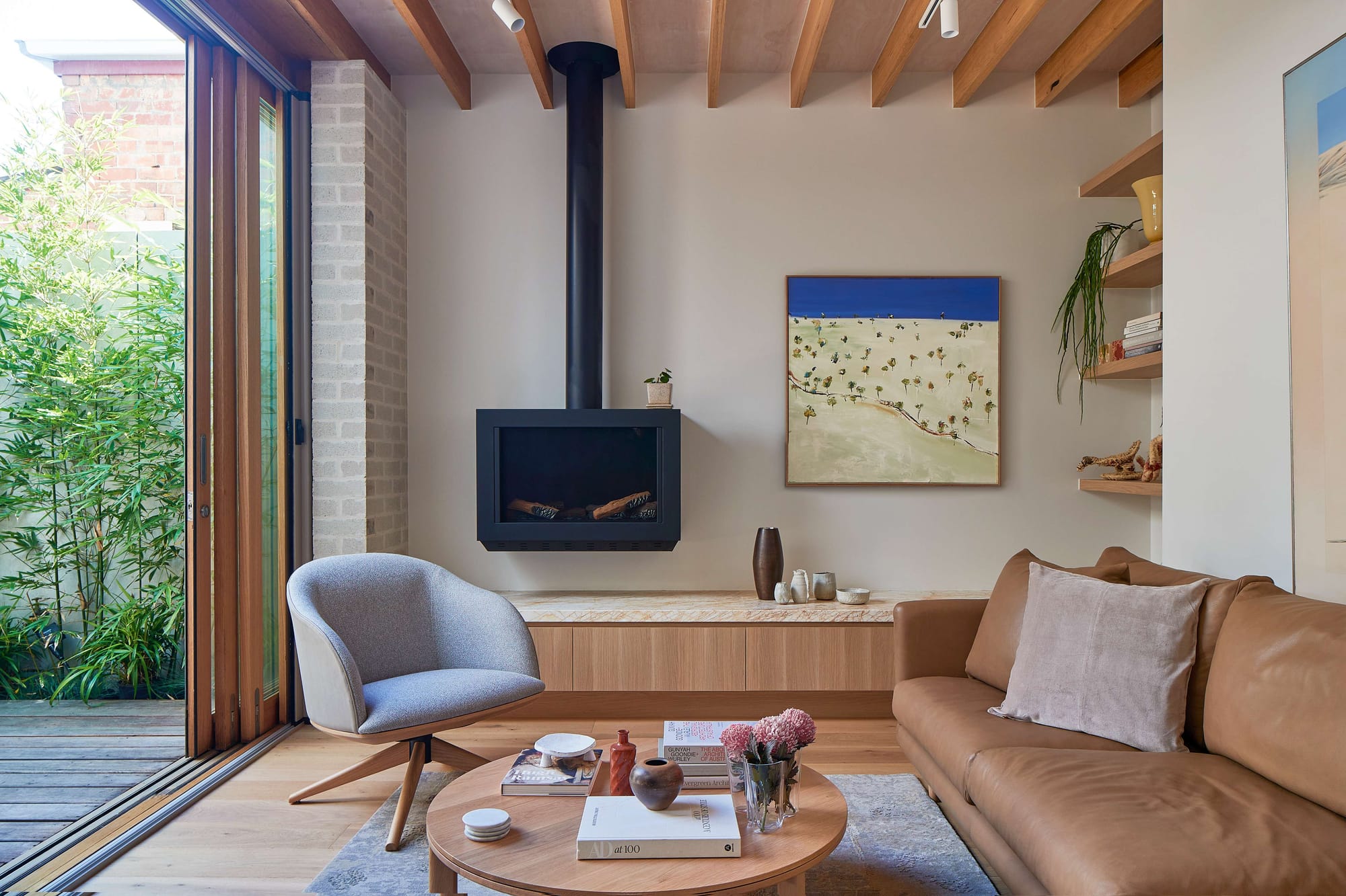 Timber-lined living room in Little OG by McMahon & Nerlich, with exposed ceiling joists, a freestanding black fireplace and sliding doors opening to the central courtyard