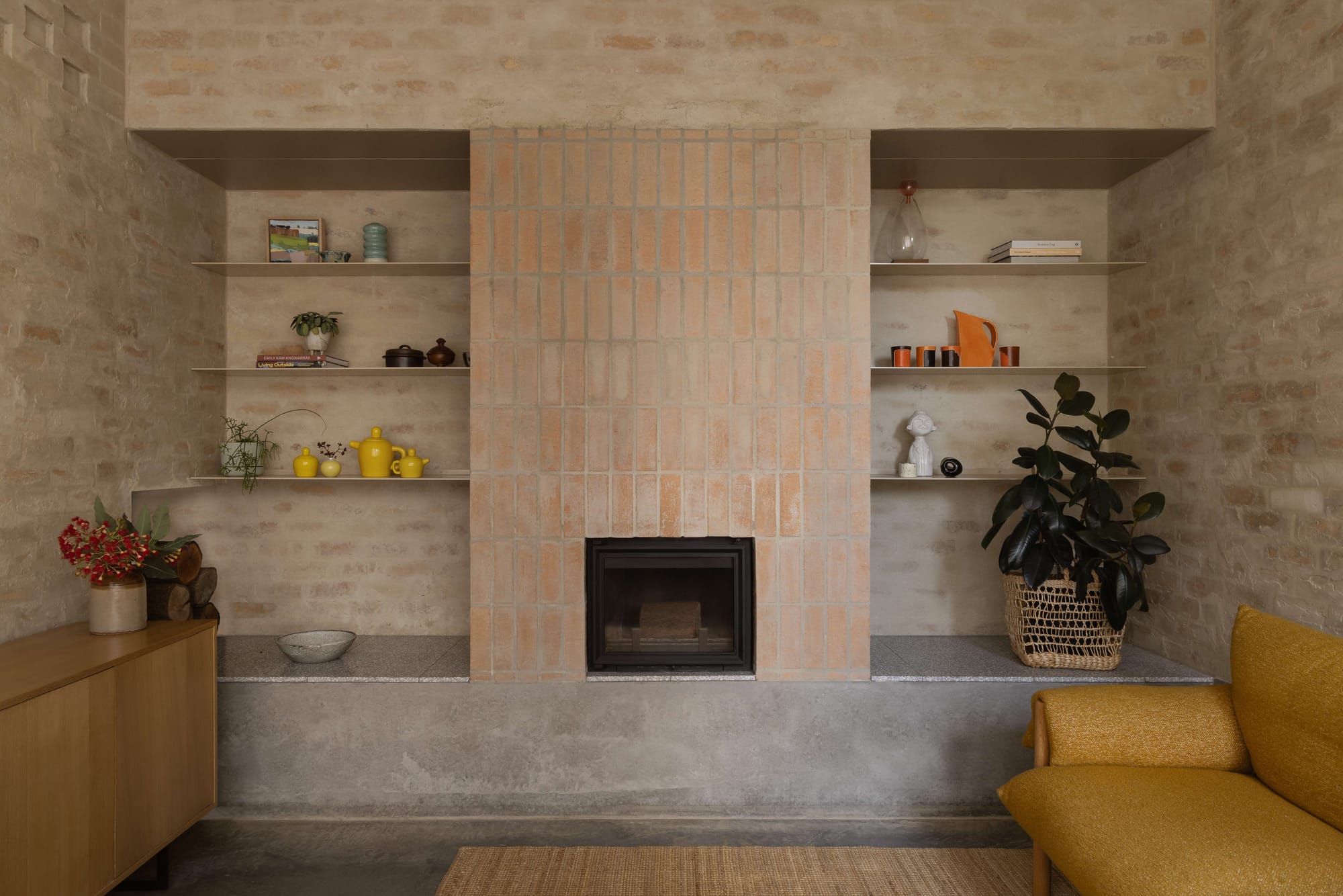 Living room fireplace with terracotta tile surround, raw stone walls, built-in shelving and polished concrete floor, Oval House by Topology Studio