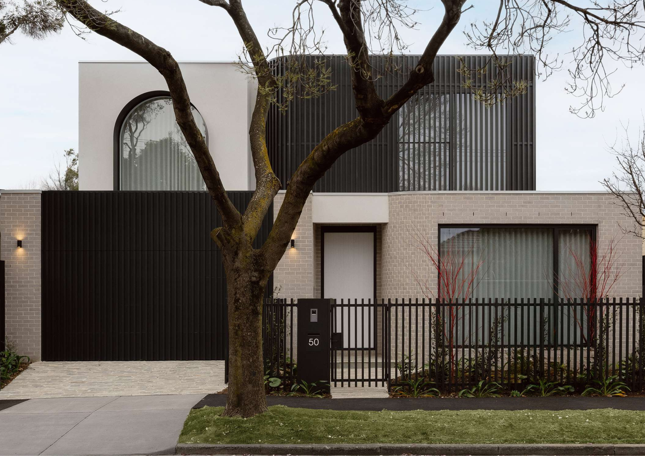 Contemporary monochrome home with curved window detailing, vertical black screening, and mature tree framing the street frontage.