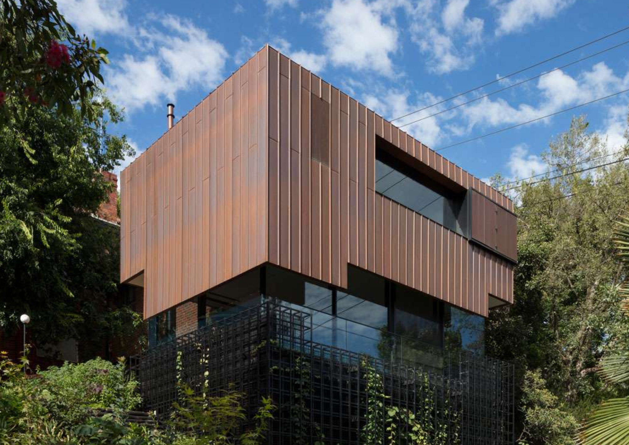 Copper-clad upper addition of South Yarra House by AM Architecture, rising above lush garden surroundings with a three-dimensional green frame visible at ground level