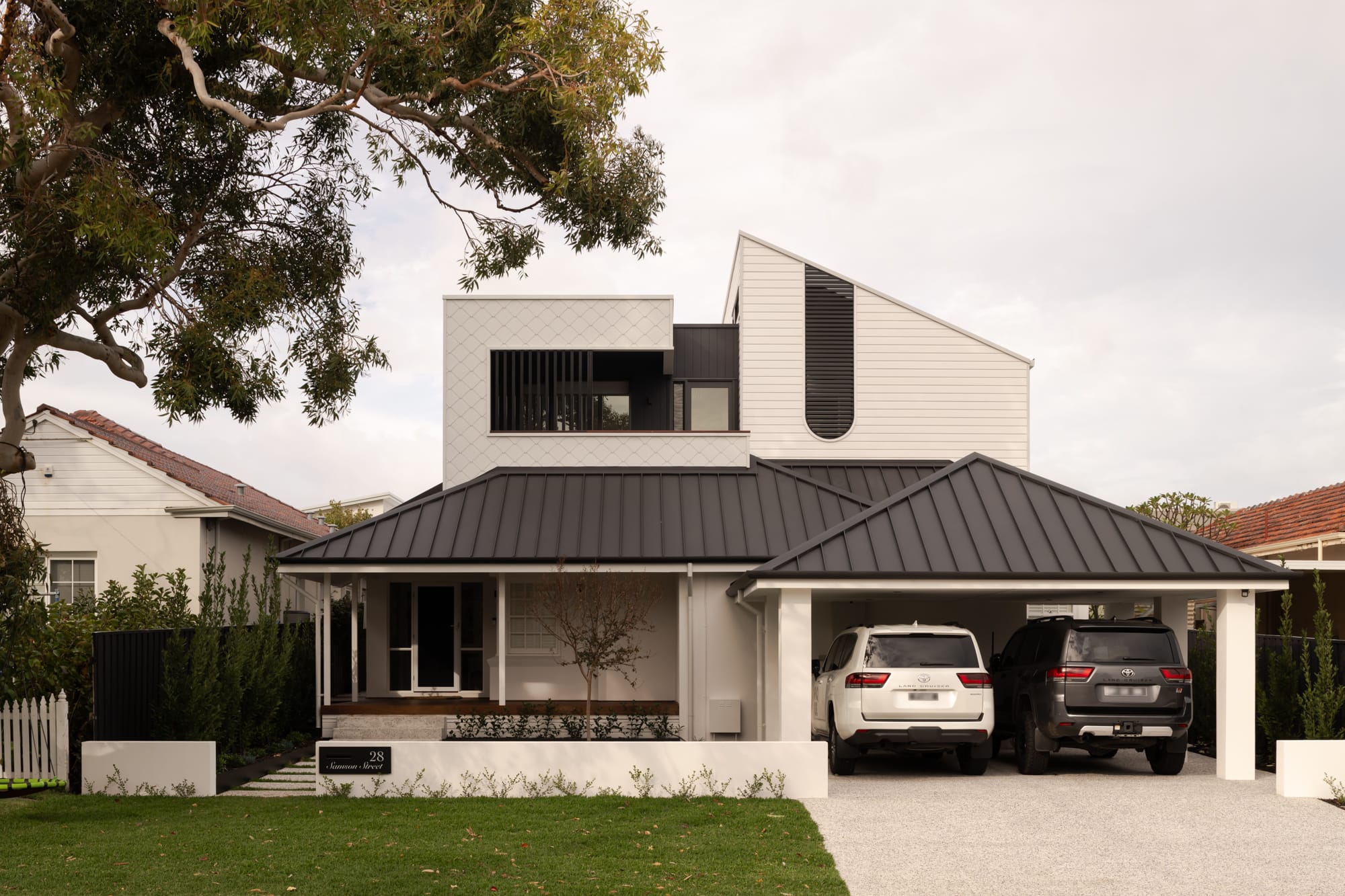 Two-storey Samson Street home by Keen Architecture with a black standing seam metal roof, white weatherboard cladding and patterned tile feature panel, set behind a heritage-style picket fence.