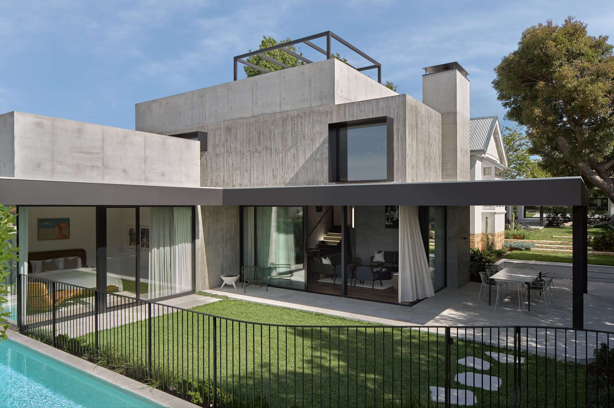 Two storey home with board formed concrete upper level, a rooftop pergola, and glass walled ground floor opening onto a lawn and pool.