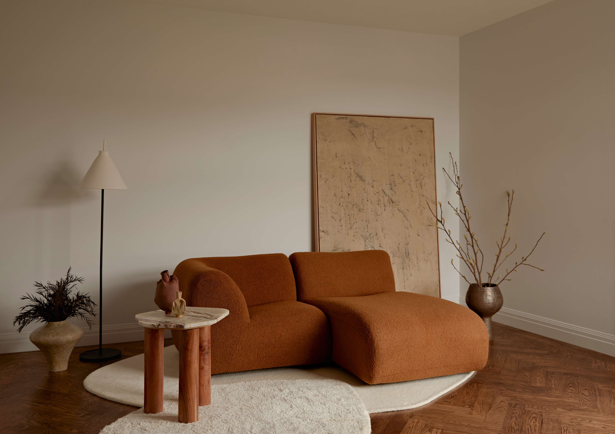 Rust coloured boucle sofa and chaise beside a timber and marble side table with ceramic vessels and framed artwork in Balwyn North by Studio Apercu