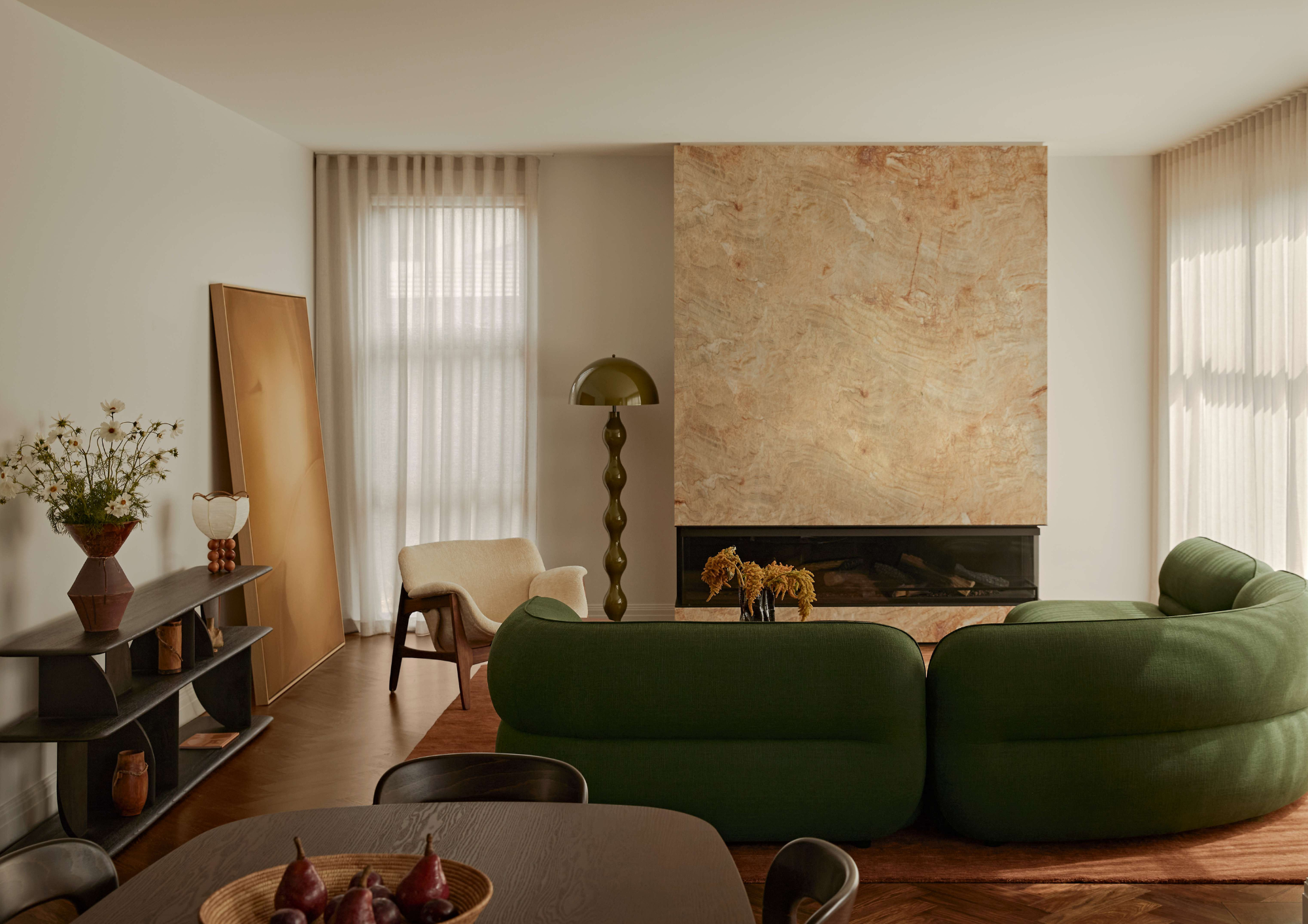 Living room with a deep green curved sofa, marble clad fireplace and sheer curtains filtering natural light in Balwyn North by Studio Apercu