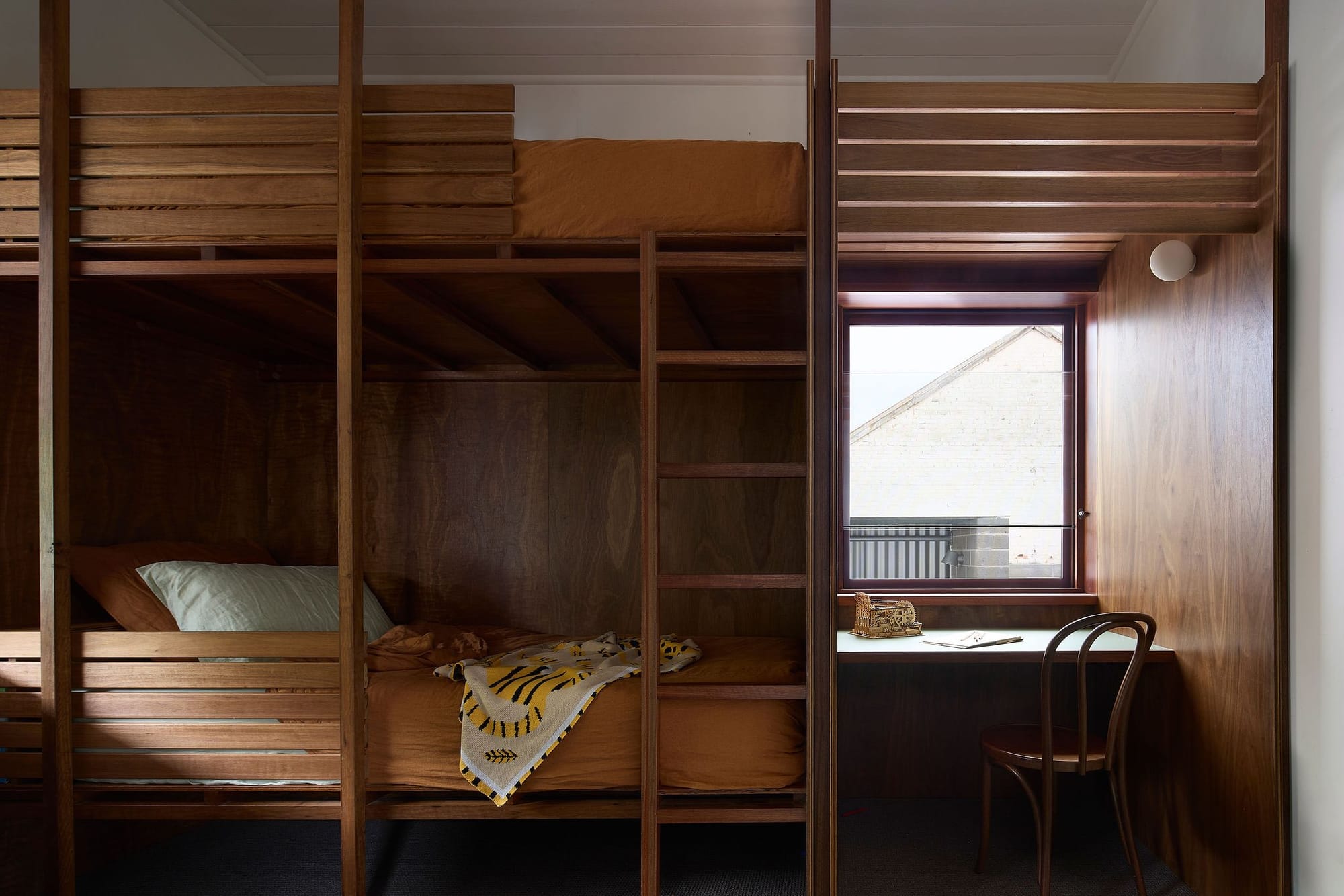 Timber bunk room with built in ladder access, a window seat desk, and a knitted throw over the lower bed.
