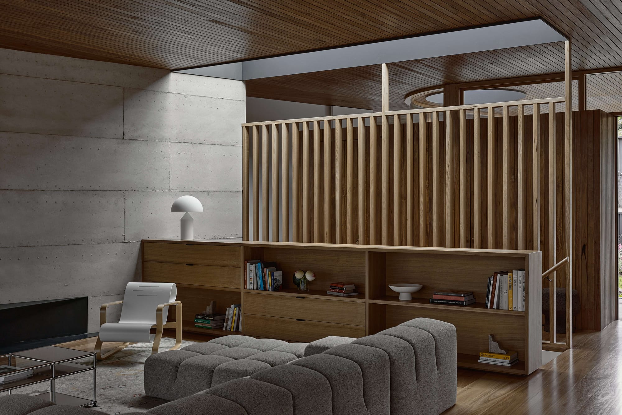 Living area with a raw concrete wall, timber slat screen, and a bouclé sofa beneath a timber panelled ceiling.