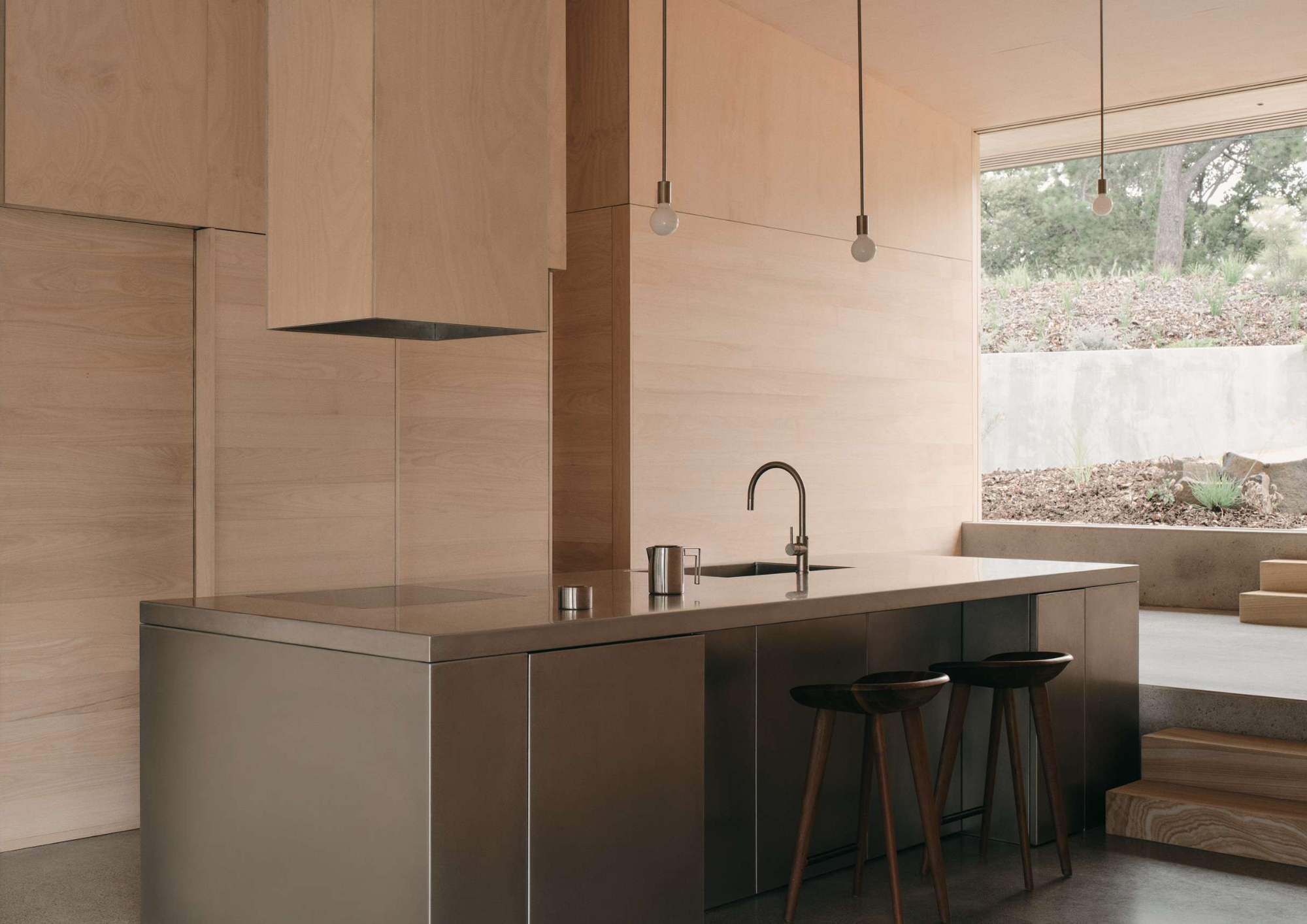 Timber panelled kitchen with a stainless steel island bench, timber bar stools and pendant lighting overlooking the landscape in Mapleton House by Atelier Chen Hung