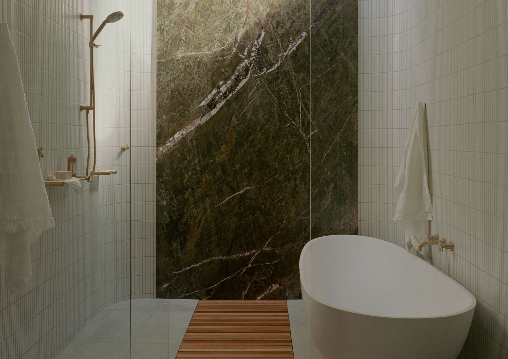 Bathroom with a freestanding stone bath, brass tapware and a striking green veined stone feature wall in Northcote Hacienda by Hindley & Co