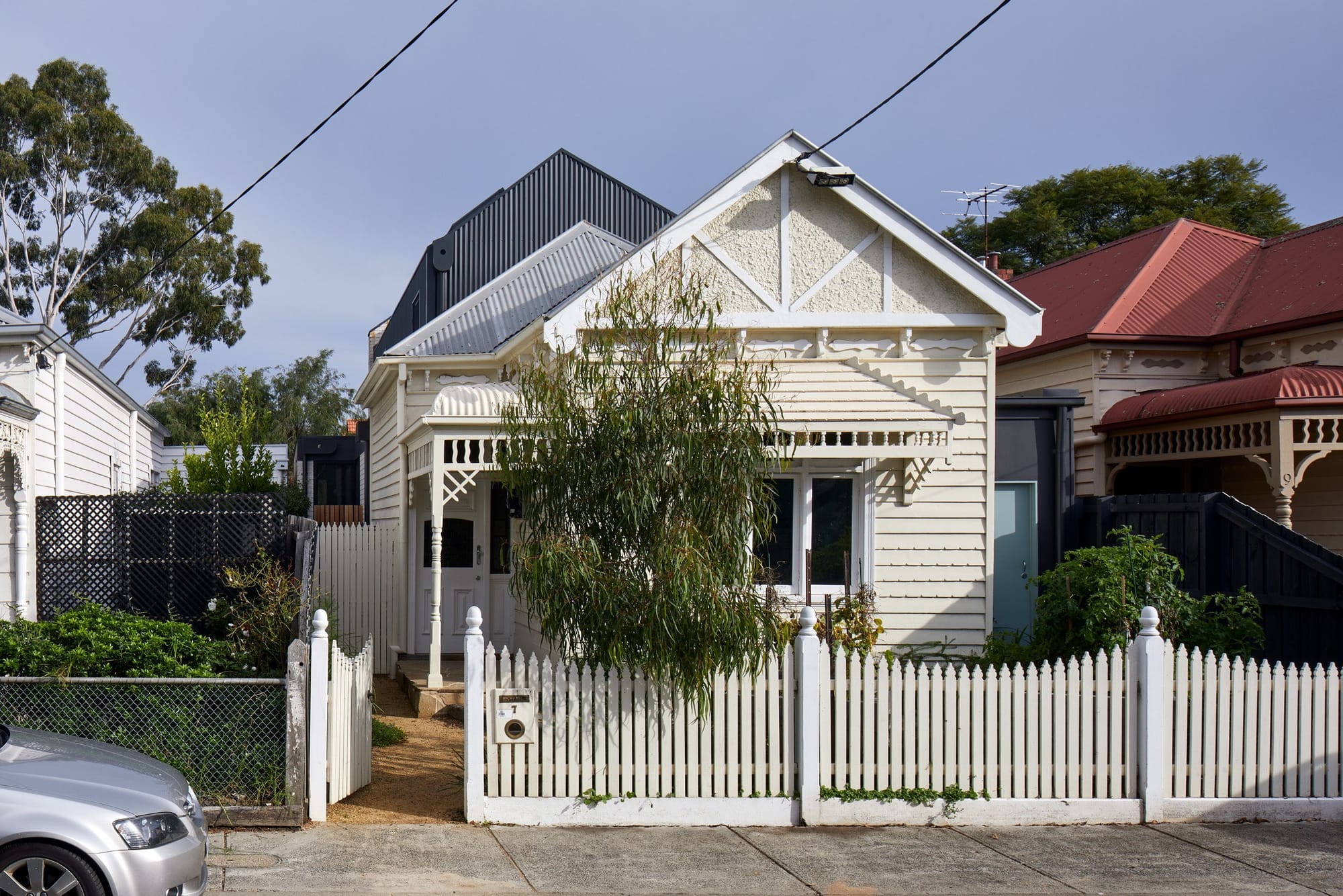Weatherboard Victorian cottage with a traditional gabled facade and a dark contemporary addition rising behind it.