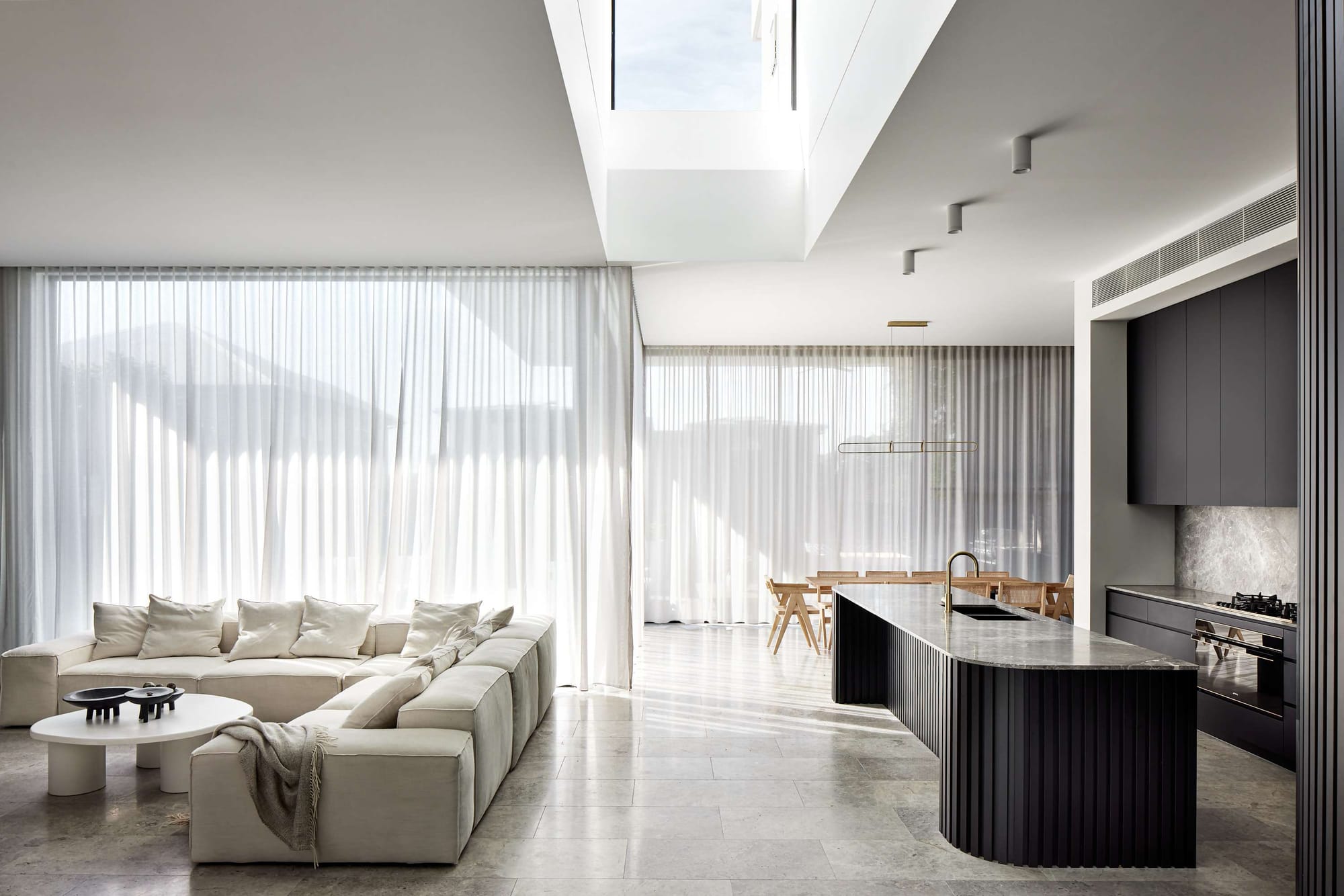 Living space with a tall skylight void above a curved fluted kitchen island, Abigail Residence by Habitat Housing