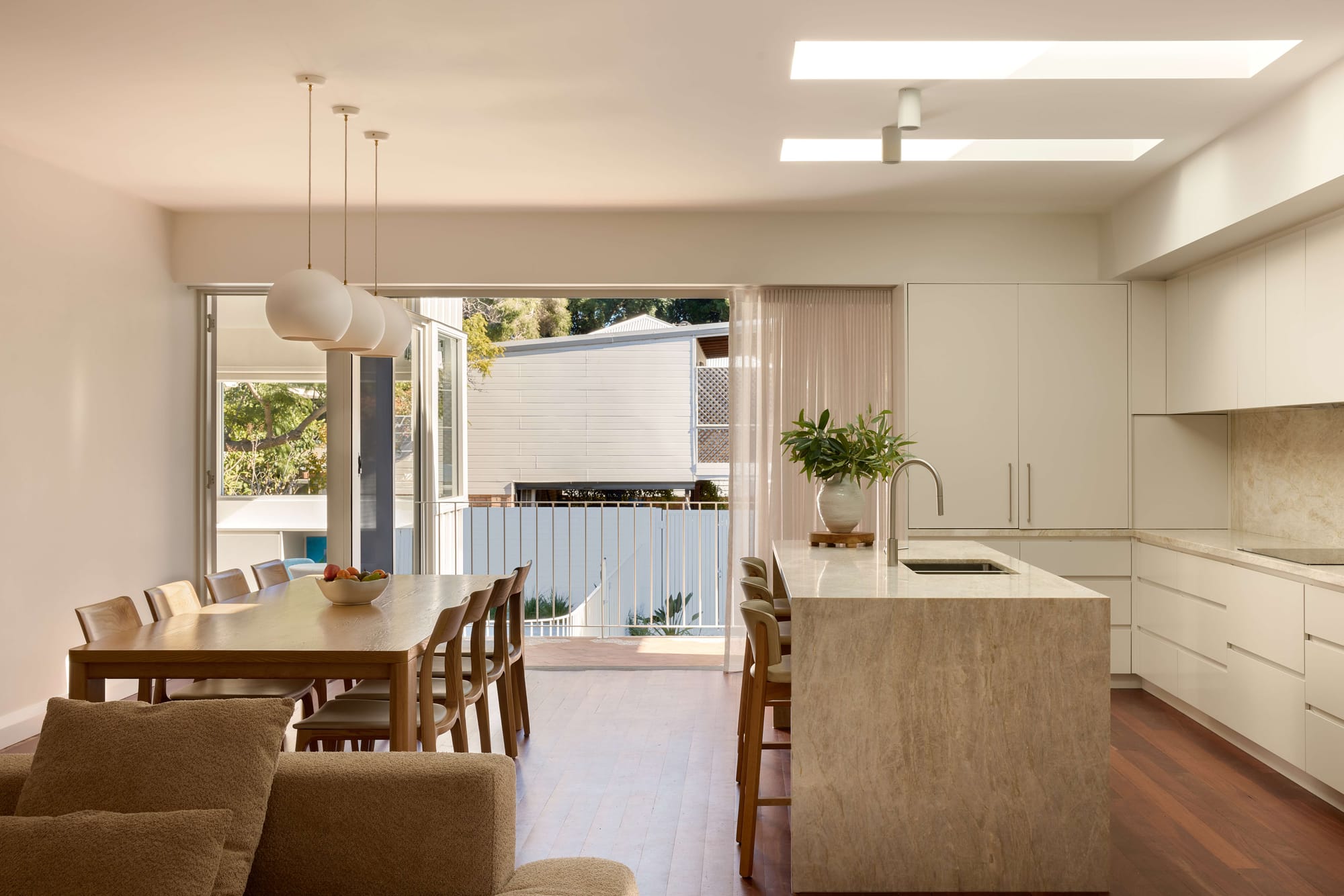 Bright open-plan kitchen and dining area with white cabinetry, a stone island, skylights and large openings connecting to an outdoor space.