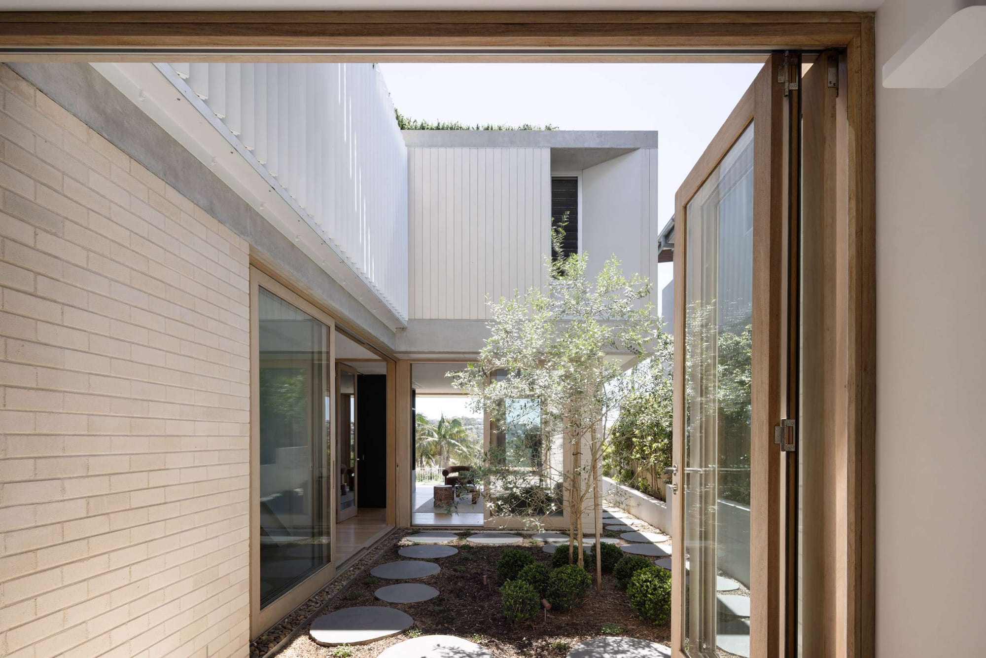 View through a sliding timber door into a courtyard garden, with the white upper storey and distant water views of Curl Curl 04