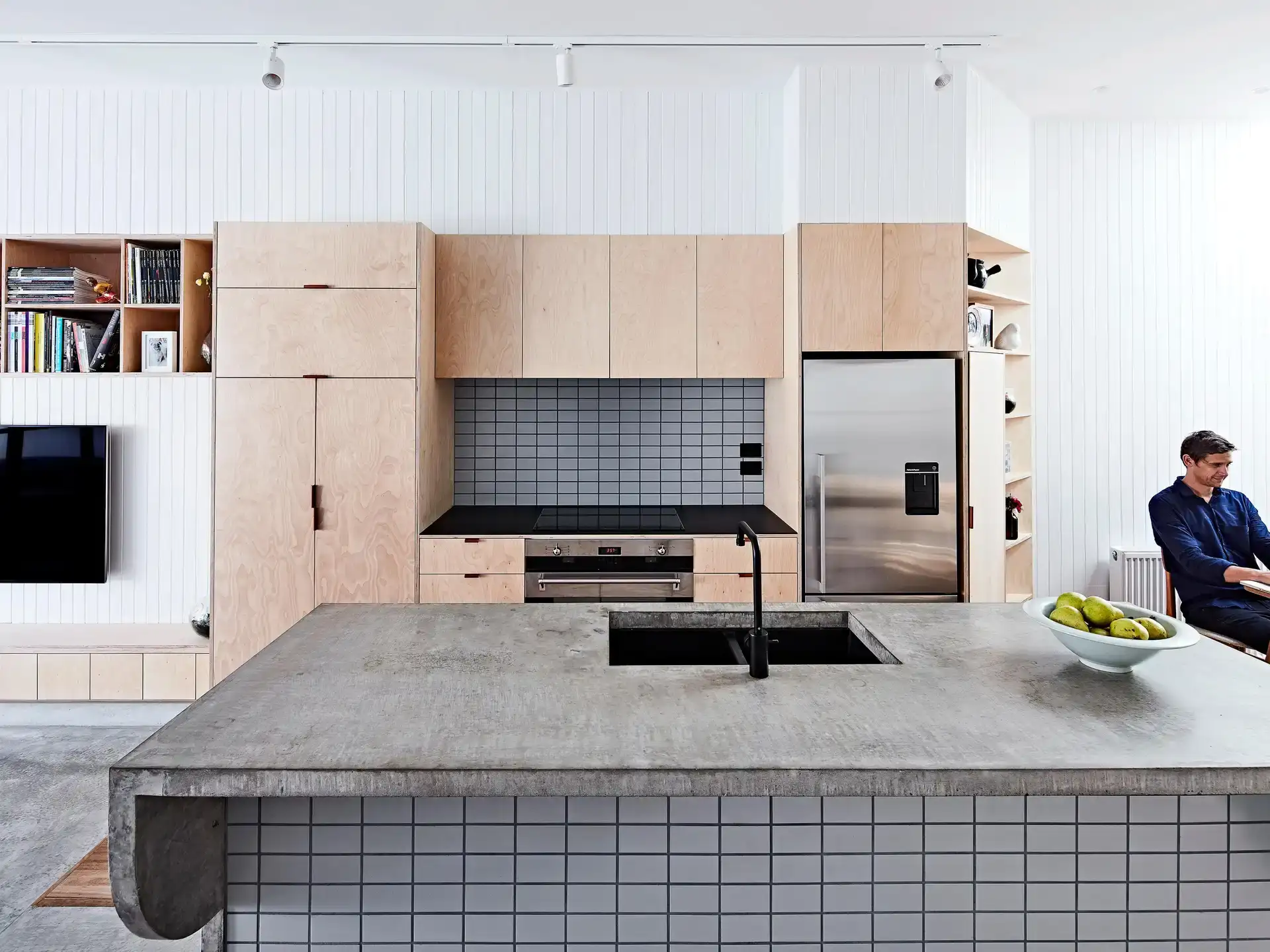 Compact kitchen at High House by True Story with plywood cabinetry, a tiled concrete island and integrated storage.