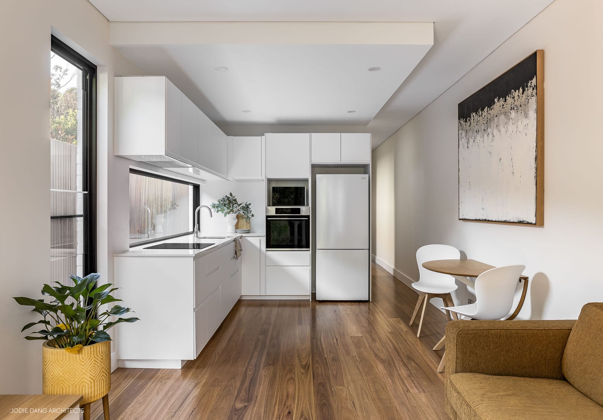 Narrow white kitchen and dining area at Leichhardt Terrace by Jodie Dang Architects with timber floors and compact built-in cabinetry.