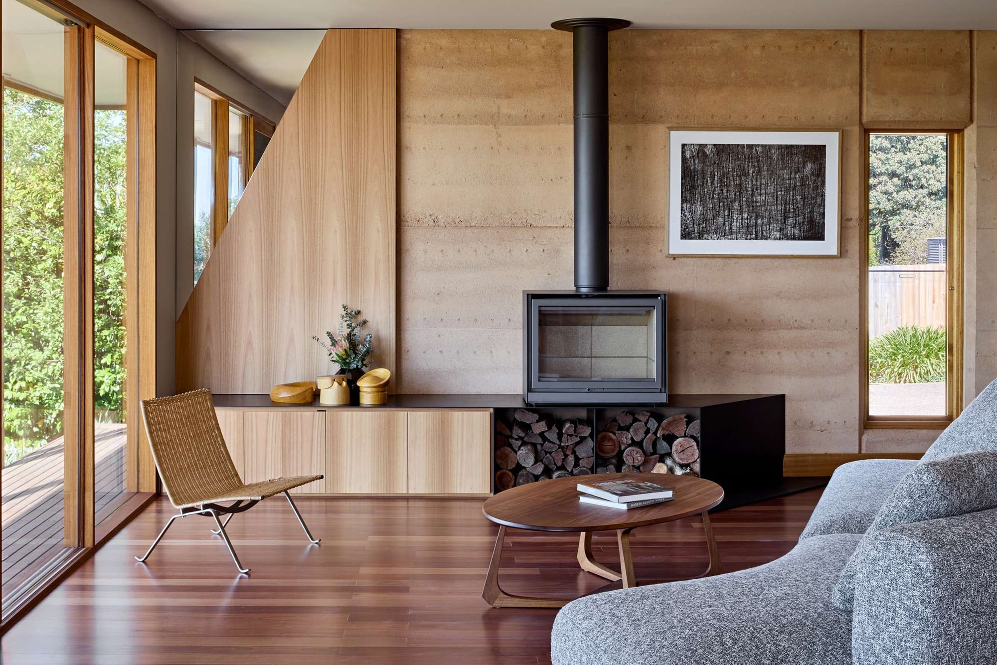 Living room at Milliner's House by FMD Architects with rammed earth walls, timber joinery, a wood-burning fireplace and garden views.
