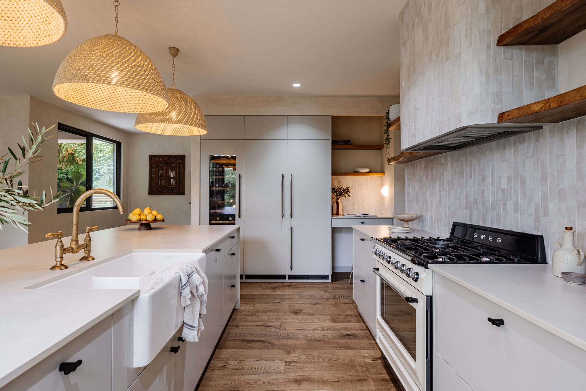 White kitchen with a large island, farmhouse sink, timber flooring, woven pendant lights and a freestanding range cooker.