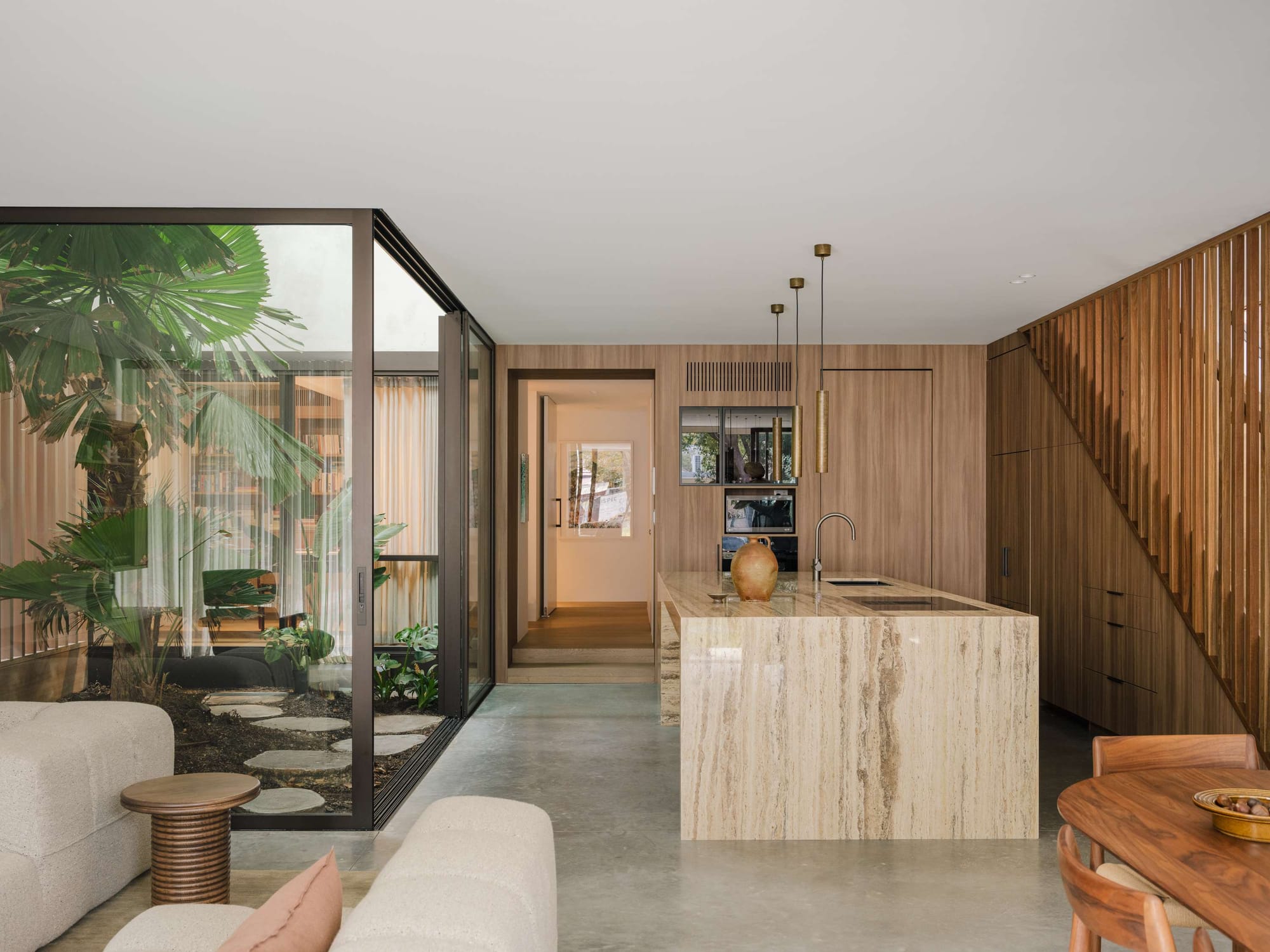 Warm timber staircase and stone kitchen bench opening onto a glazed courtyard filled with palms, Petersham House
