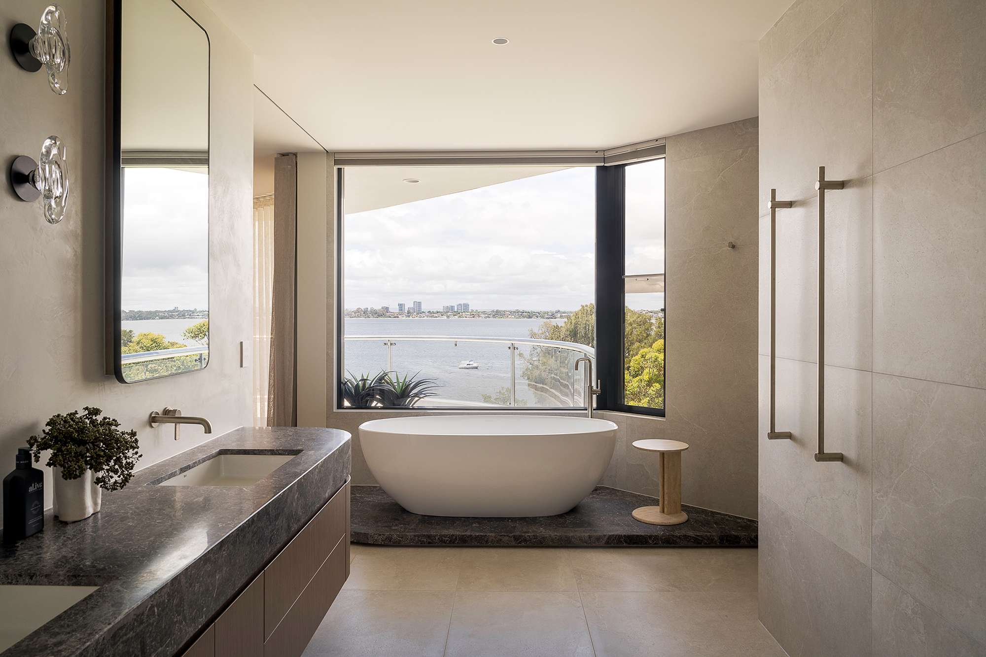 Penthouse bathroom by Lux Interiors with a freestanding bath, stone vanity and large windows overlooking the water.