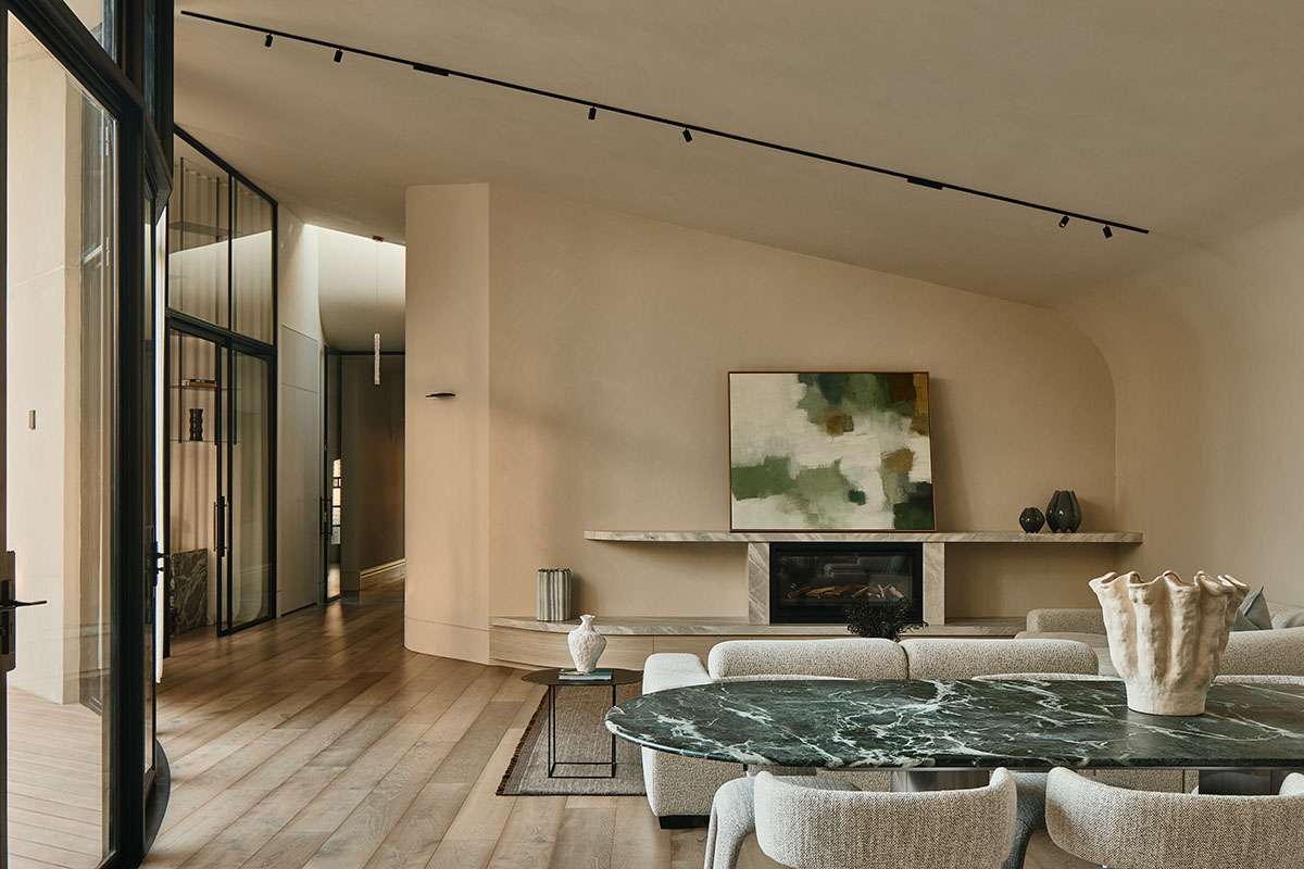 A warm, curved living room with a marble-topped fireplace, abstract green artwork, boucle sofas, and a green marble dining table in the foreground.
