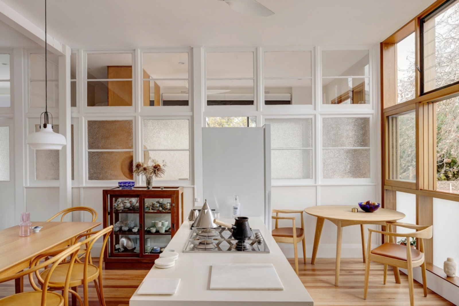 Kitchen and dining area at Dempsey Warehouse, with a white island, timber floors and furniture, and glazed partitions sharing natural light.