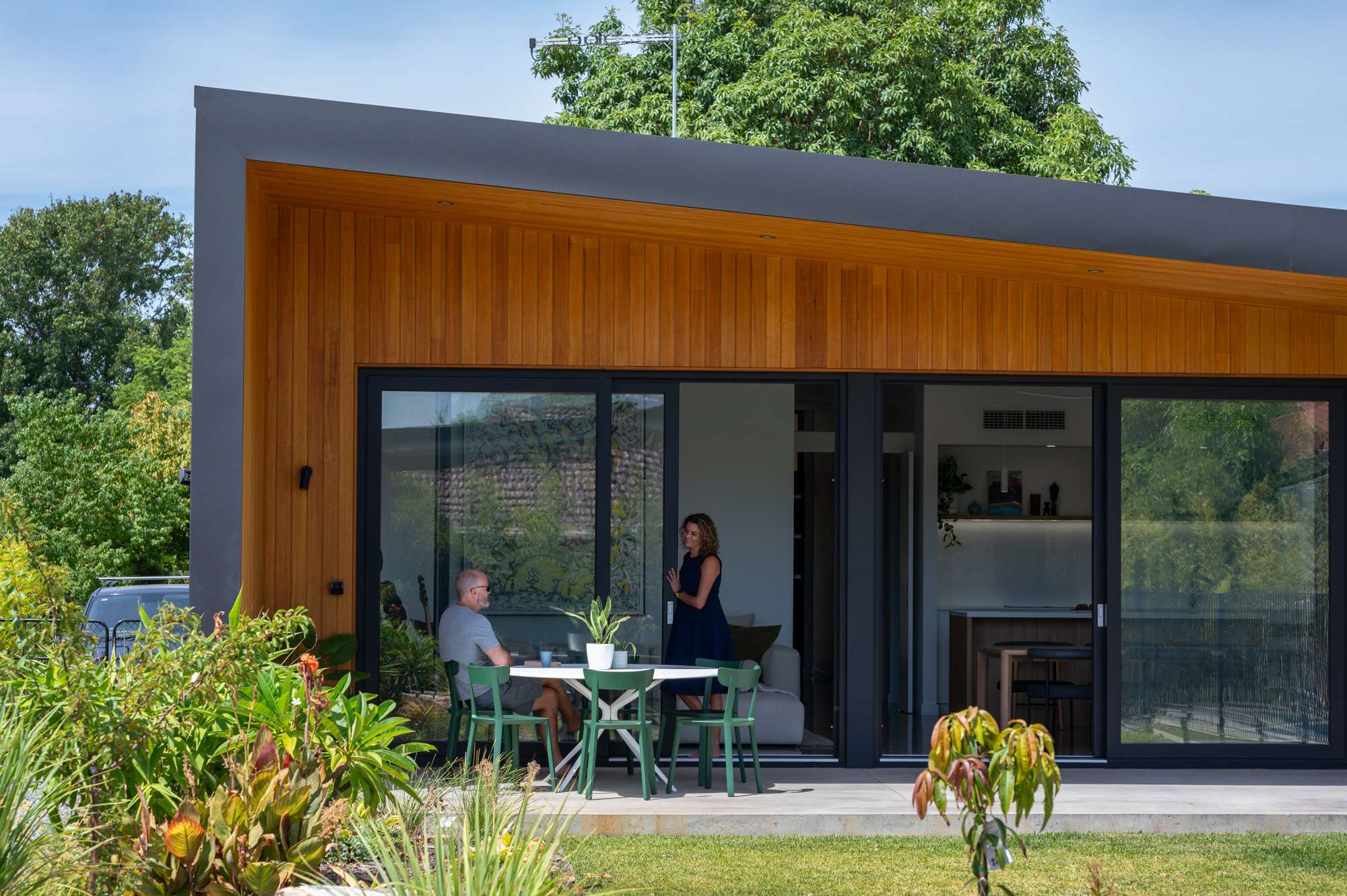 Timber-clad extension with an angled skillion roof and glass sliding doors opening to a garden courtyard with outdoor seating, by Leanhaus.