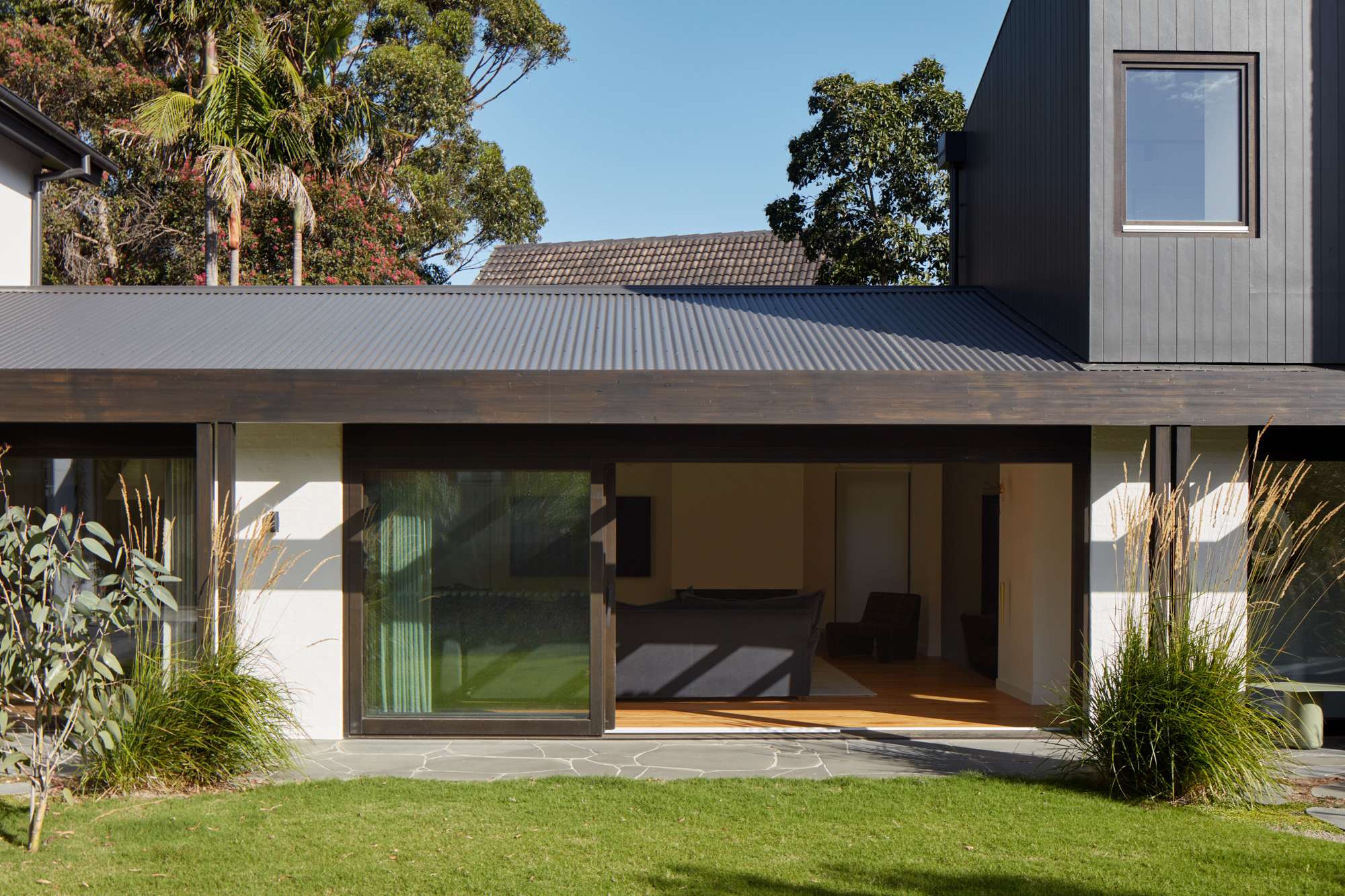 Rear extension with dark cladding and wide sliding glass doors opening from the living room onto a stone terrace and lawn.