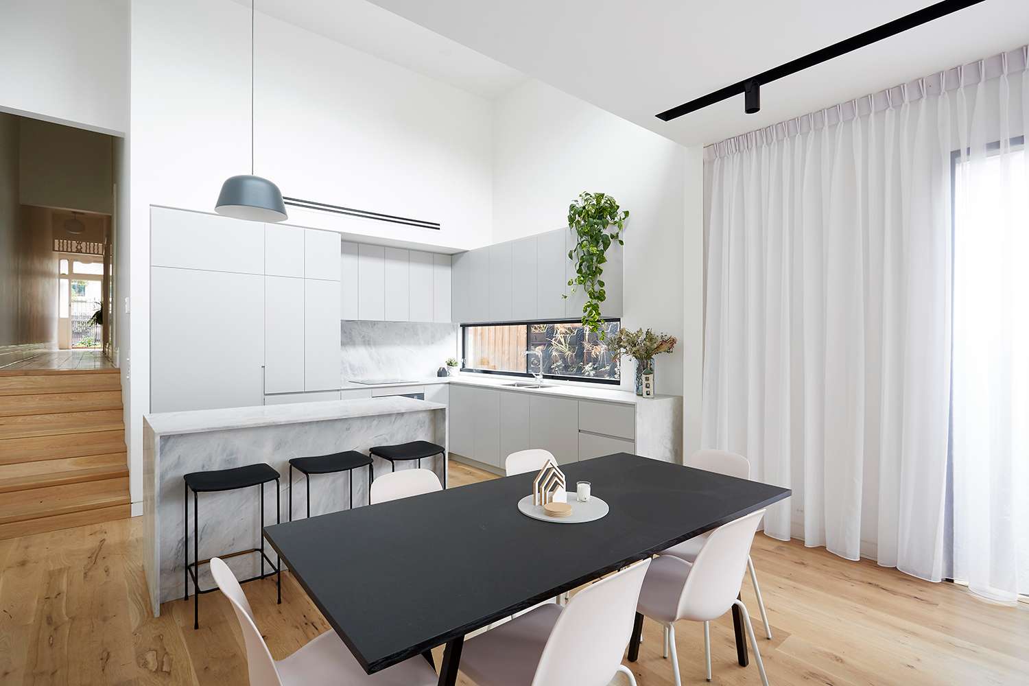 Light filled kitchen and dining area at Charles Street Residence by Haussegger Interiors, with pale joinery, stone surfaces and warm timber flooring.