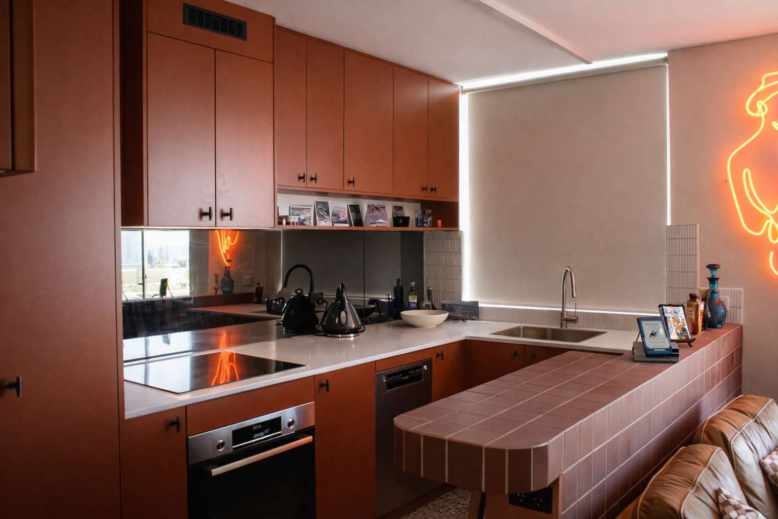 Compact kitchen by Michael Folk Architects and Interiors with rust coloured cabinetry, white benchtops and a tiled island overlooking the living area.