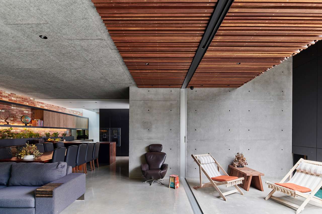 Concrete and timber living area at Carlton Lanes End in Melbourne by UrbanID, with sliding glass doors connecting the interior to a sheltered courtyard.